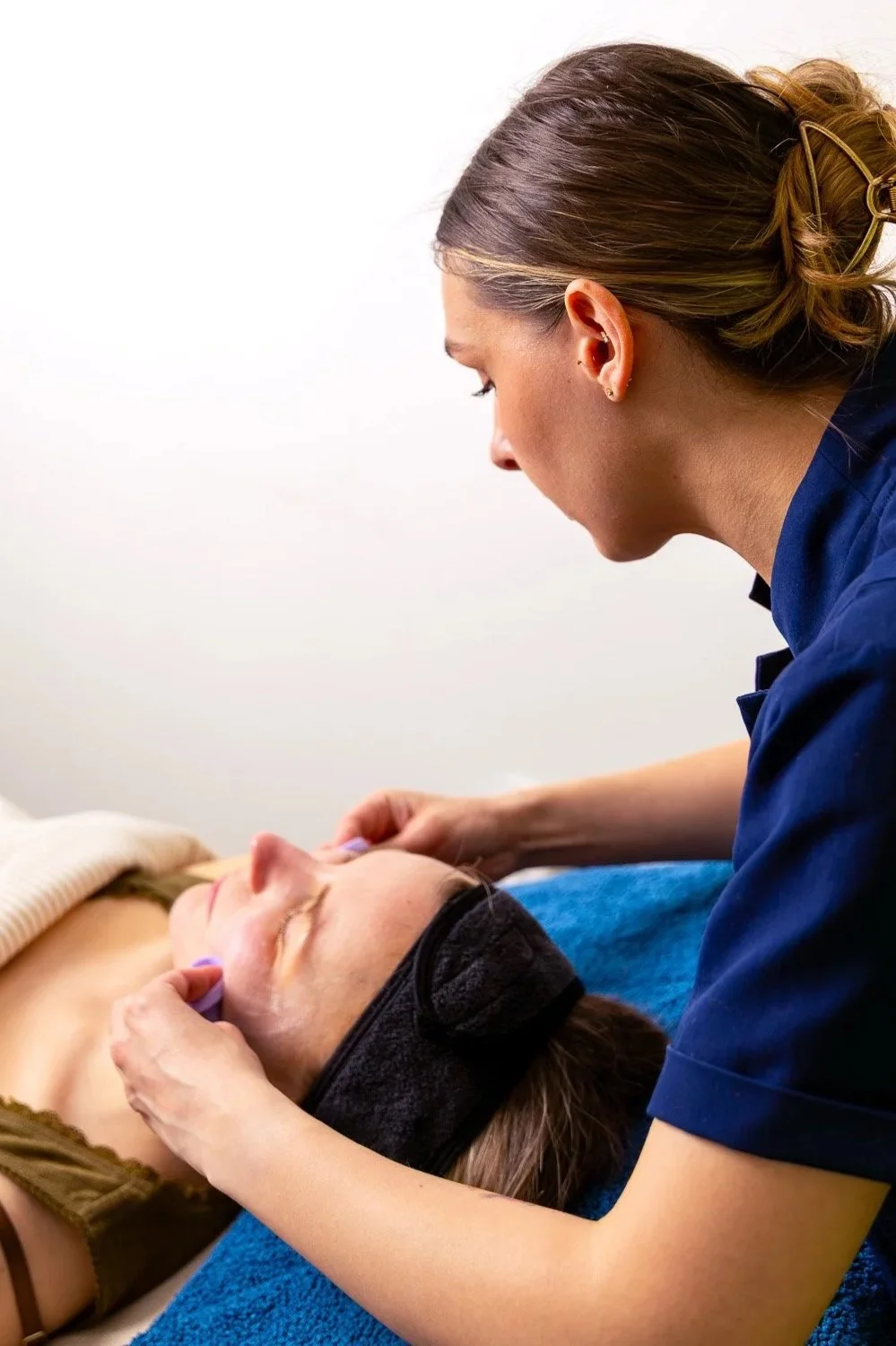 A woman receiving a facial massage or skincare treatment from a esthetician in a professional setting.