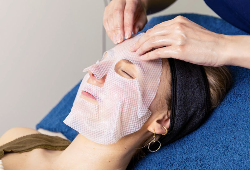A woman receiving a facial treatment with a sheet mask applied to her face during a spa session.