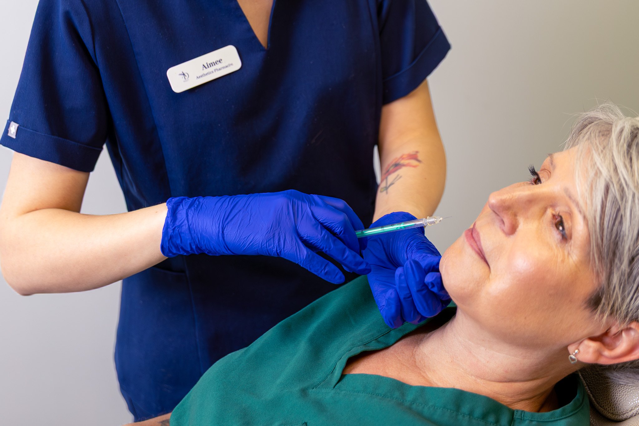 A healthcare worker administering a shot to an elderly woman lying down in a medical setting.