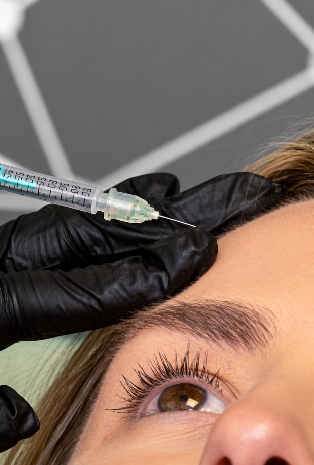 A person receiving an eyebrow injection or treatment with a syringe held by a gloved hand, close-up of their face showing brown eye and eyebrow.
