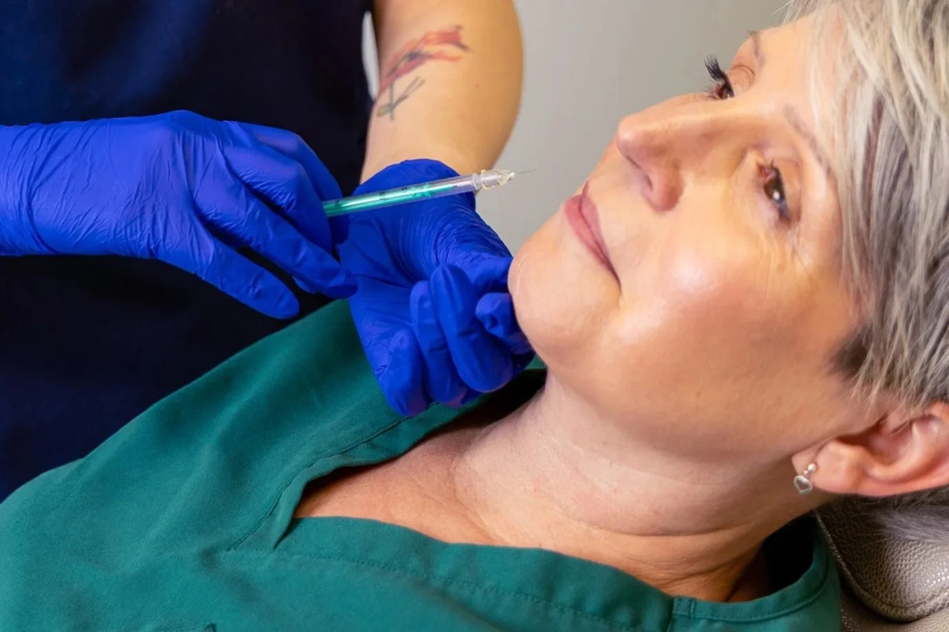 A woman receives a cosmetic injection in her cheek from a medical professional wearing blue gloves.