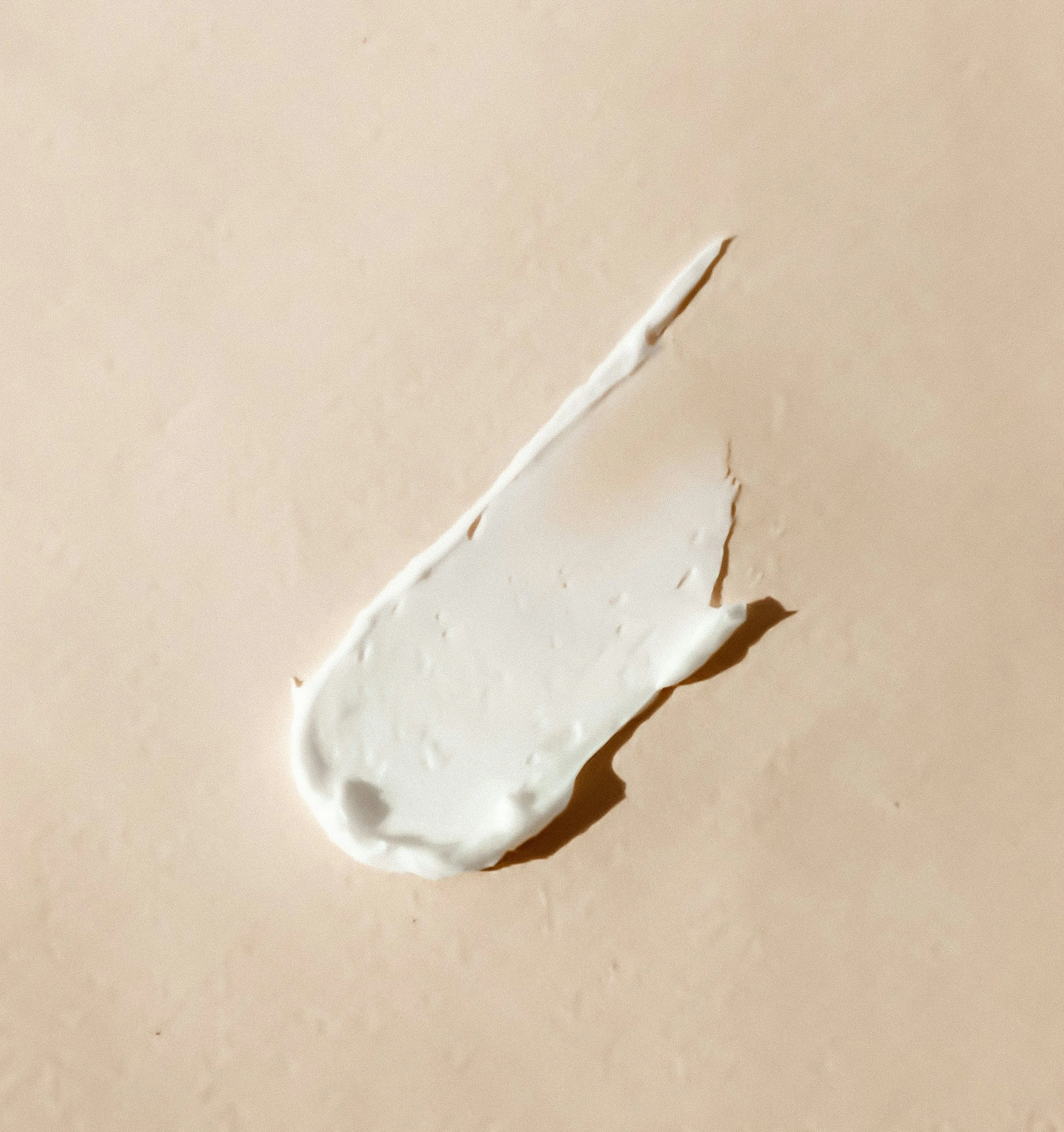 Close-up of a torn piece of white paper with rough edges, lying on a plain beige surface.