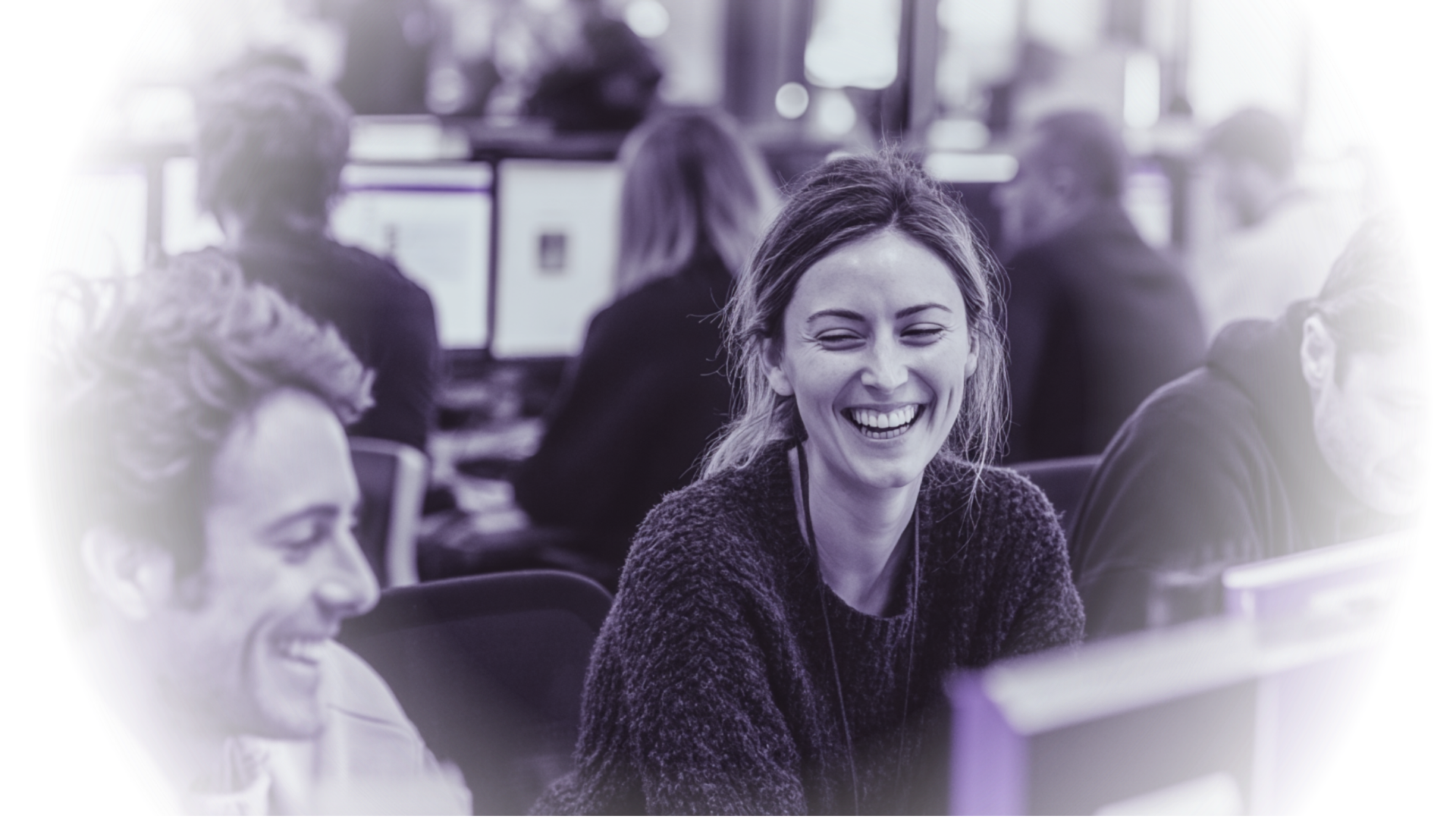 Office workers in a busy workspace, smiling and working at their computers.