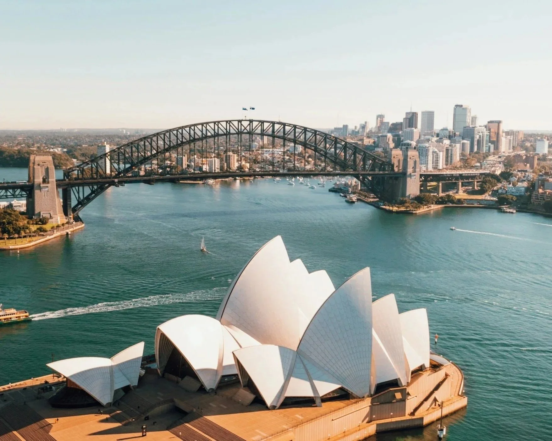 Aerial view of Sydney Opera House with Sydney Harbour Bridge in the background, city skyline, and boats on the water.