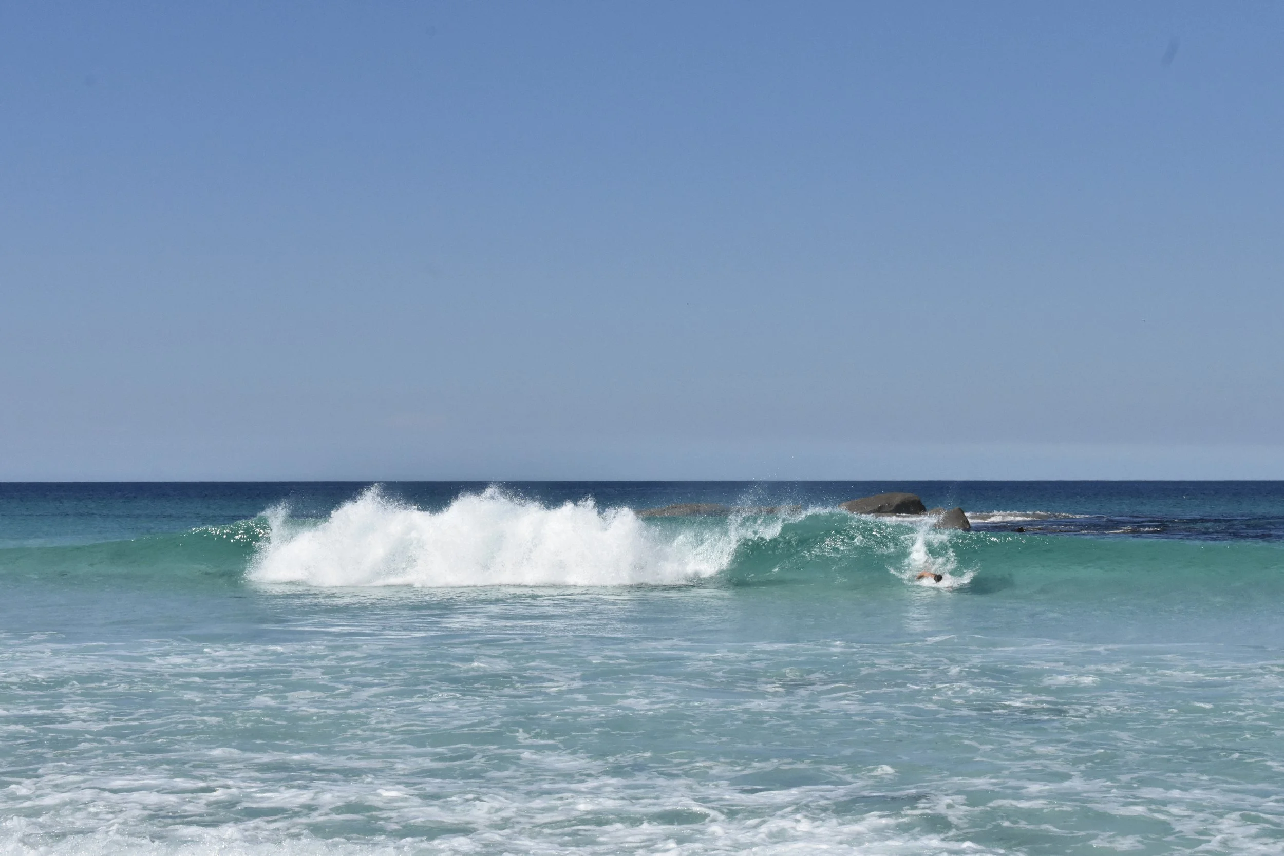 Waves crashing on the shore of a beach with blue sky and horizon in the background.