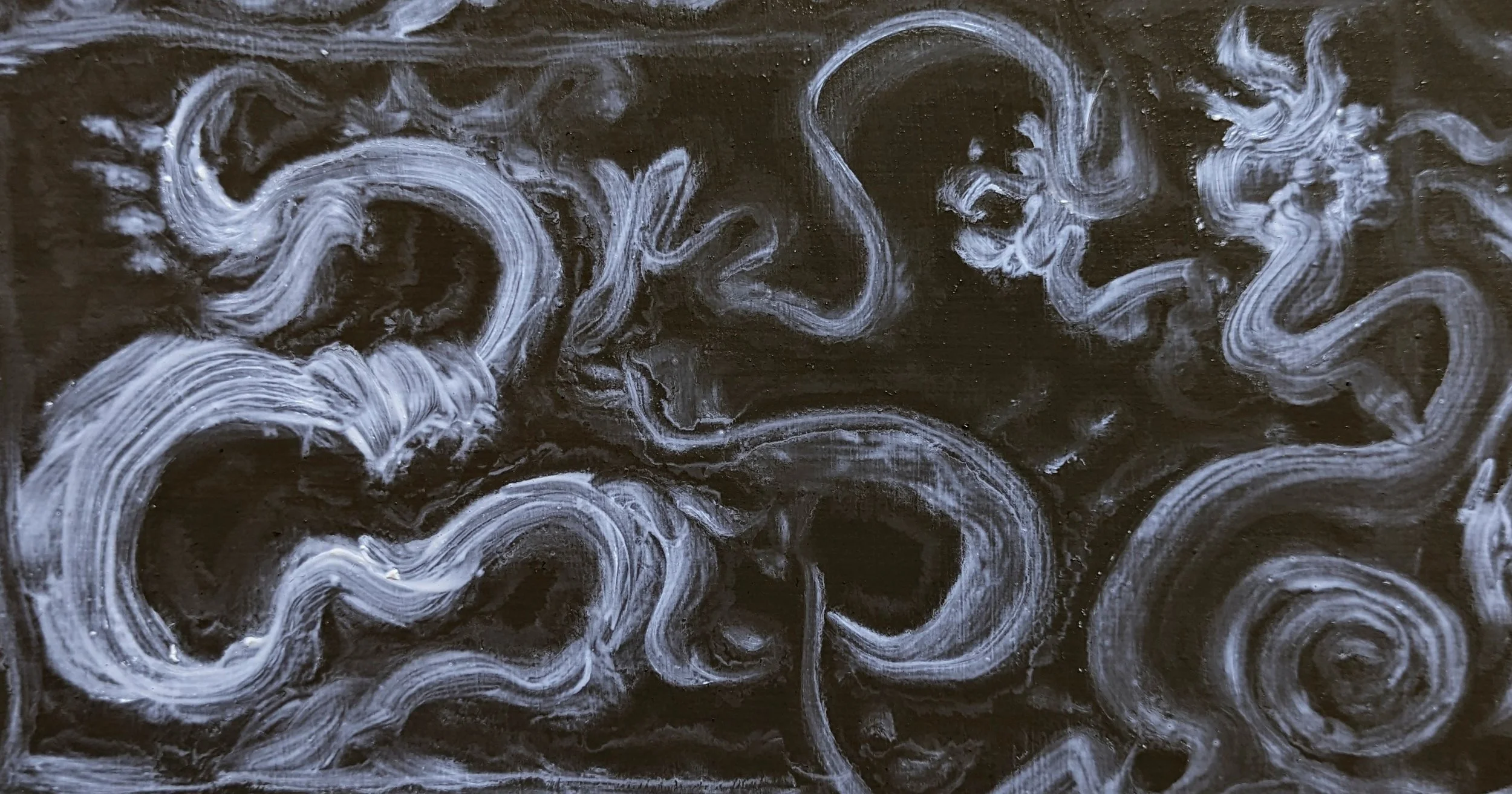 Close-up of a dark surface with swirling white chalk or paint lines creating abstract patterns.