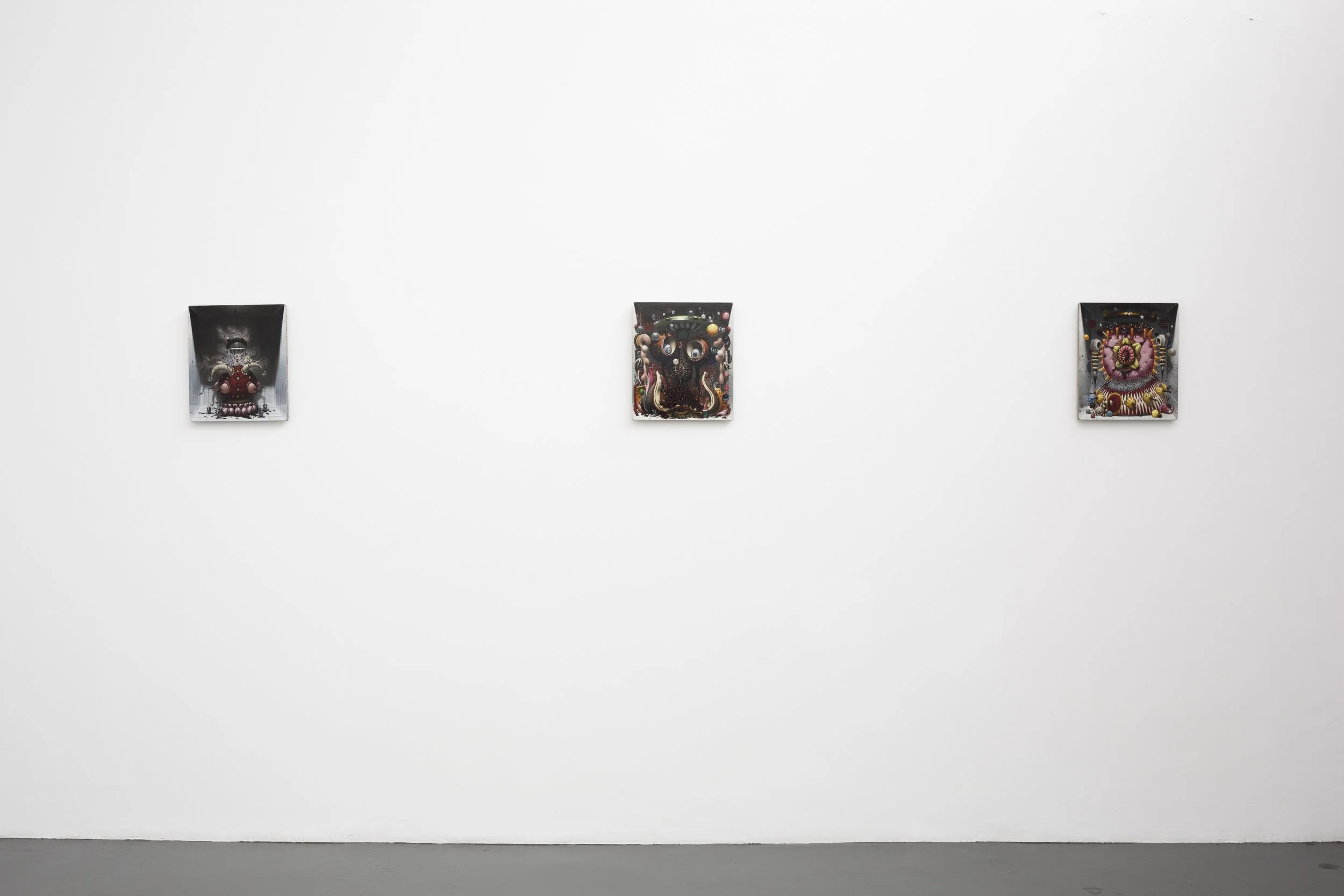 Three small colorful art pieces displayed on a white gallery wall.