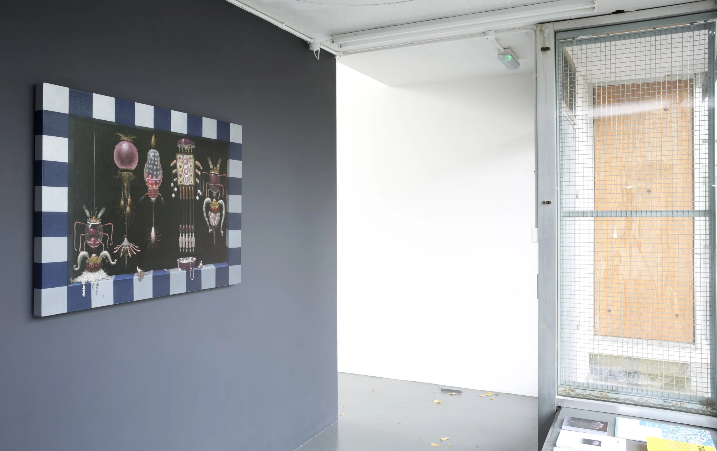 An art gallery corner with a colorful artwork on the gray wall and a window door with a metal grid, letting in natural light.