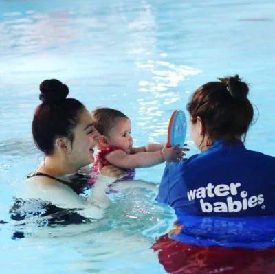 A water safety instructor teaching a young girl to swim using a mirror at a swimming pool.