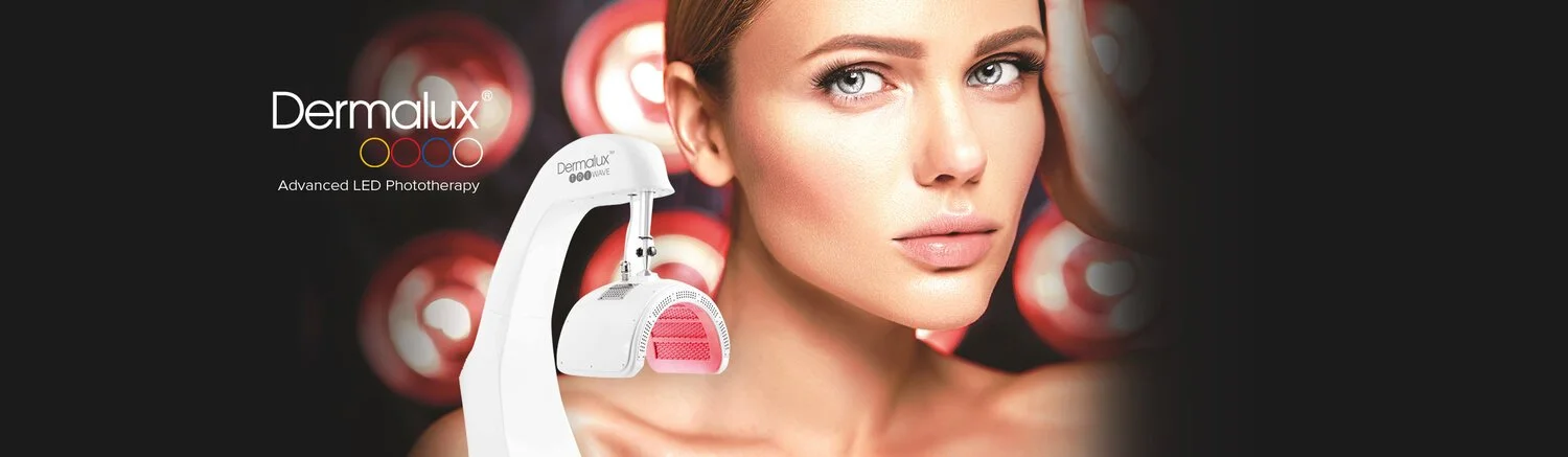 A woman looks directly at the camera with clear skin, positioned outdoors or against a dark background with circular lights. There is a Dermalux LED phototherapy device in front of her, indicating a skincare treatment setting.