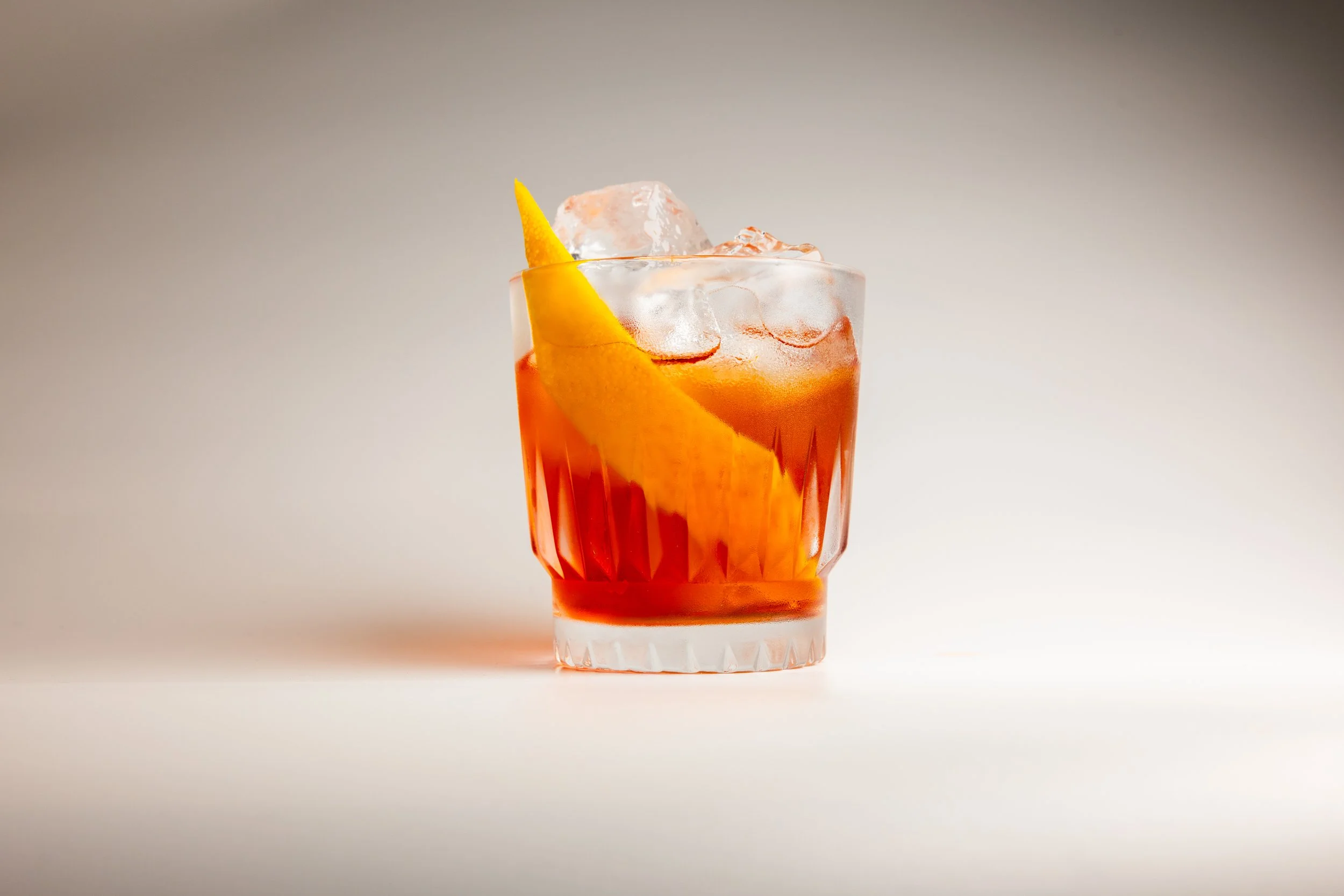 A glass of orange-colored cocktail with ice cubes and an orange peacock placed inside.