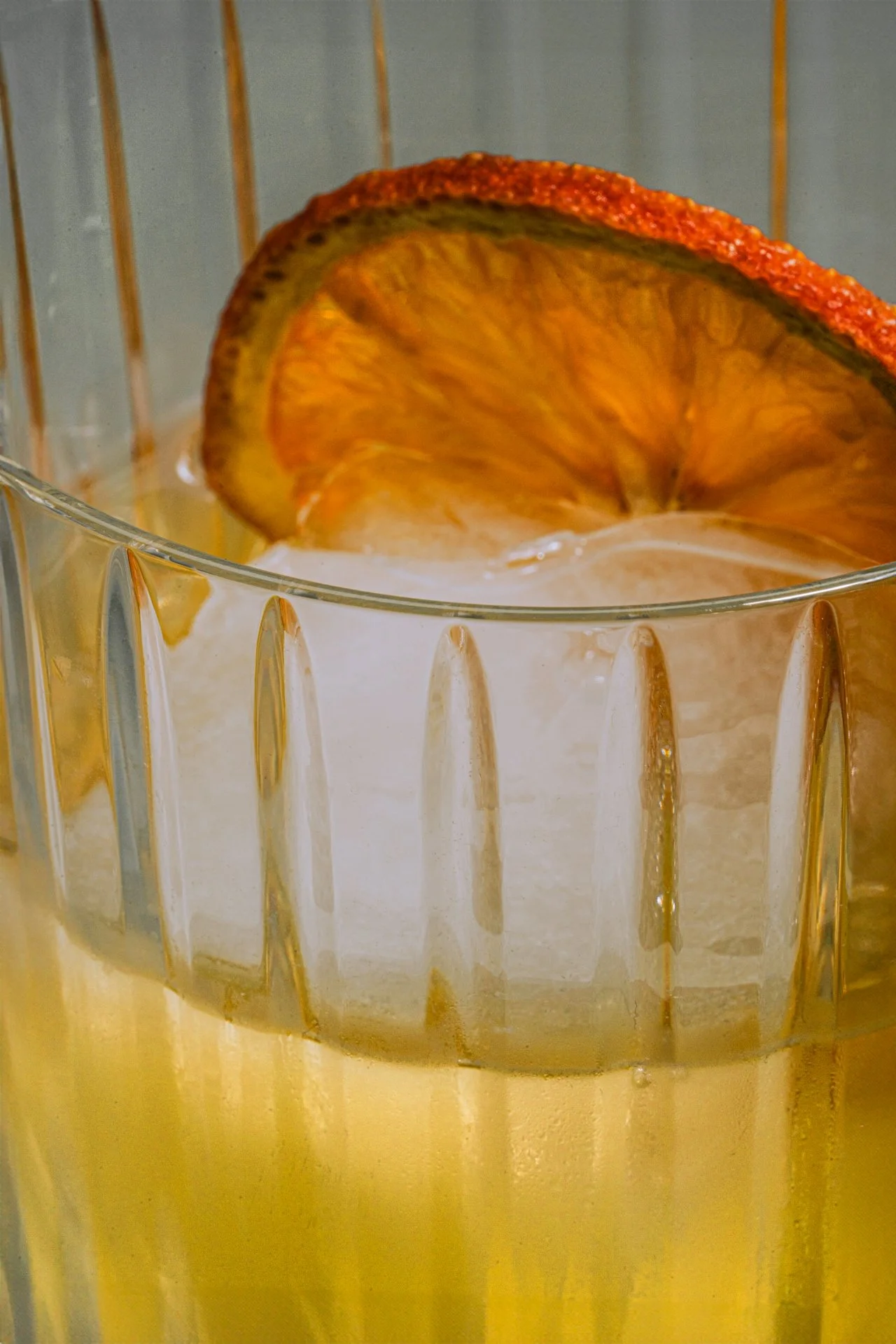 Close-up of a glass of yellow drink with a slice of dried citrus fruit on the rim.
