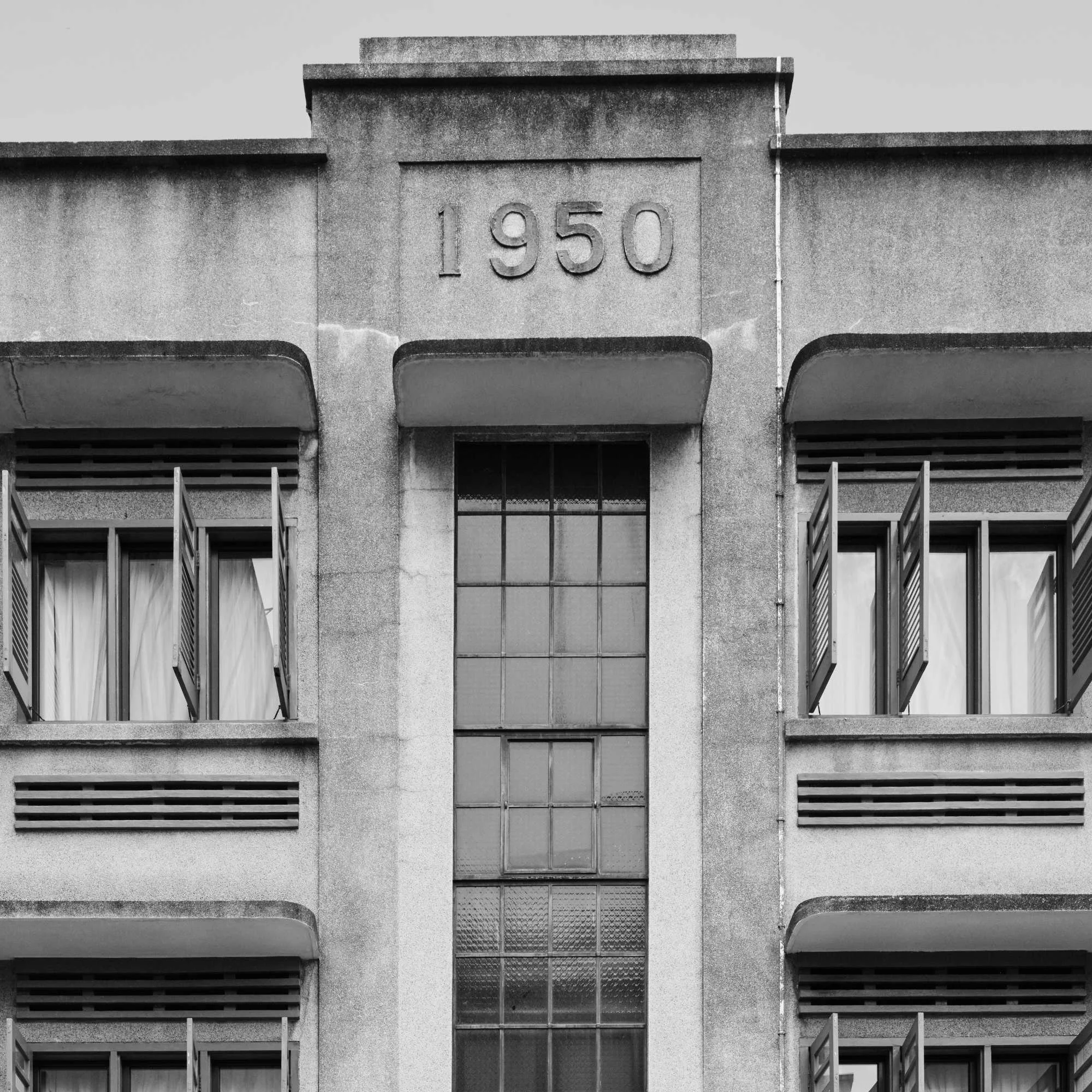 Black and white image of a building's facade with the year 1950 engraved on a central column.