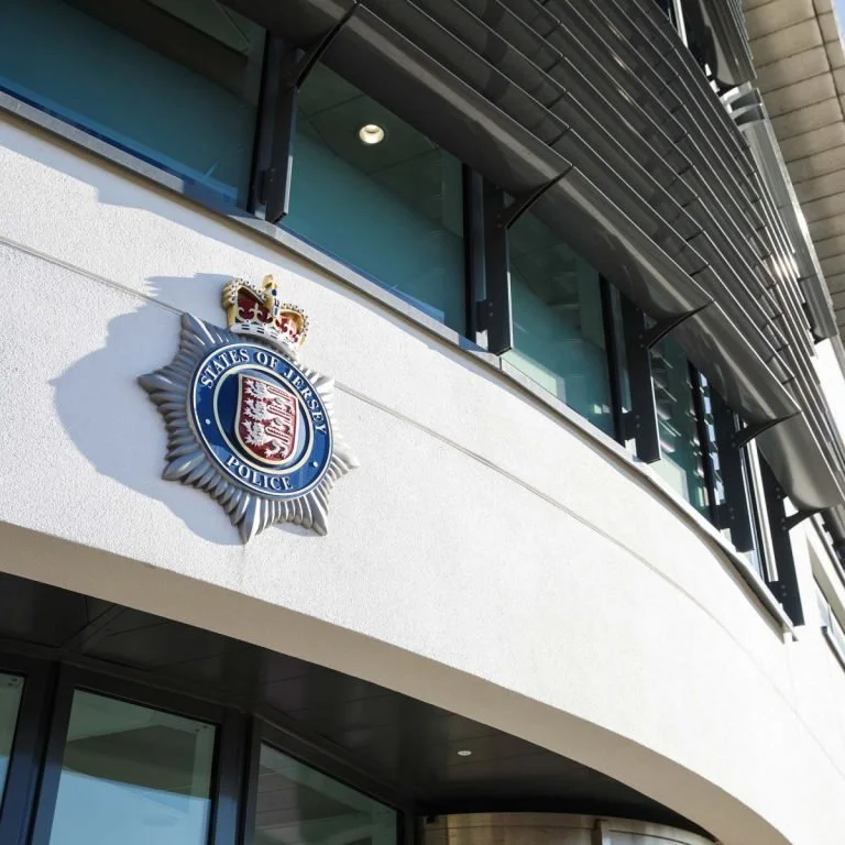 Exterior of a government building with a police emblem featuring a crown, shield, and the text 'States of Jersey Police' on the wall.