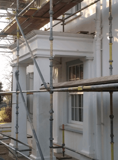 Exterior of a building under construction or renovation, with scaffolding surrounding a white wall and a window.
