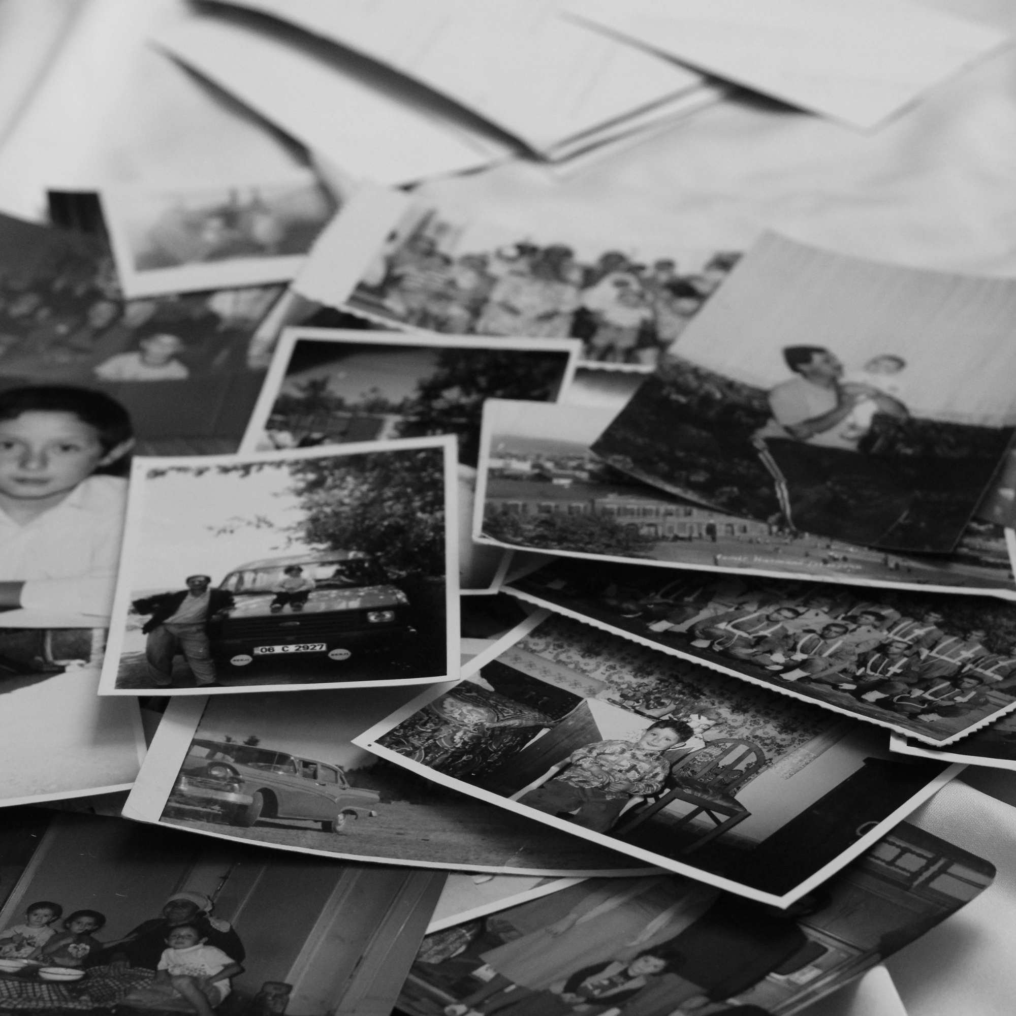 A pile of scattered black and white photographs, some overlapping, showing various people, likely family members or friends, in different settings and poses.