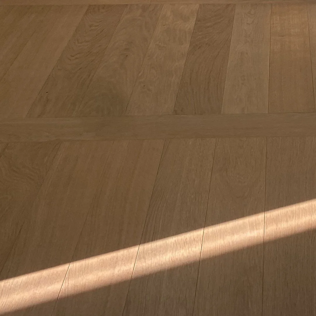 Close-up of a wooden floor with a section illuminated by sunlight, creating a bright beam across the surface.