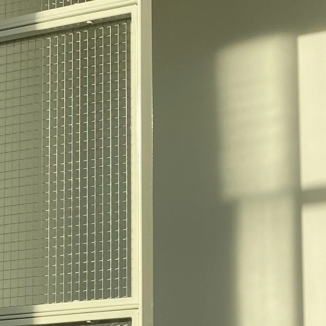 Sunlight casting a rectangular shadow on a plain wall, next to a metal cabinet with a grid pattern.