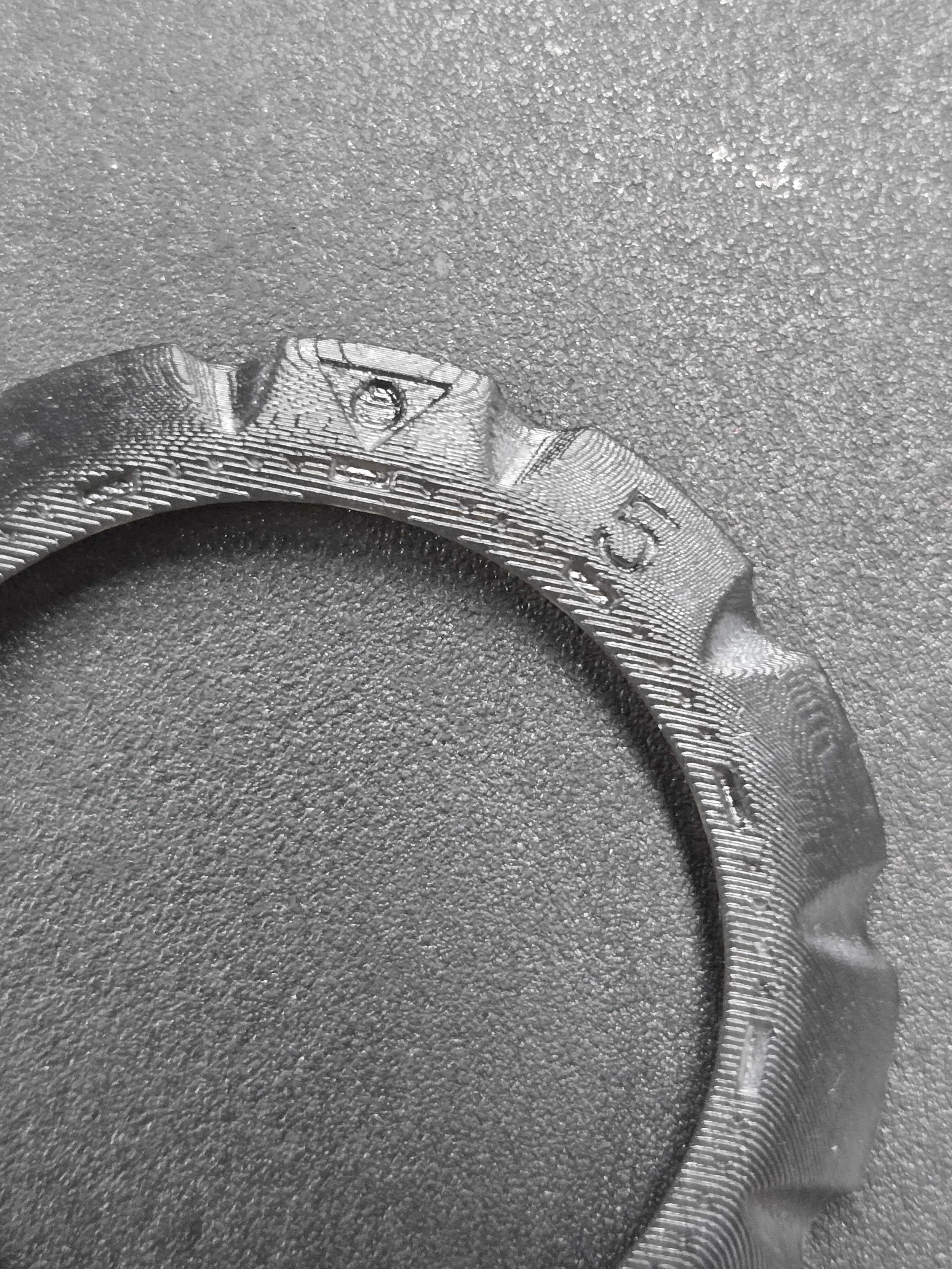 Close-up of a silver dollar coin with the eye of the Illuminati symbol engraved on it, lying on a textured dark surface.