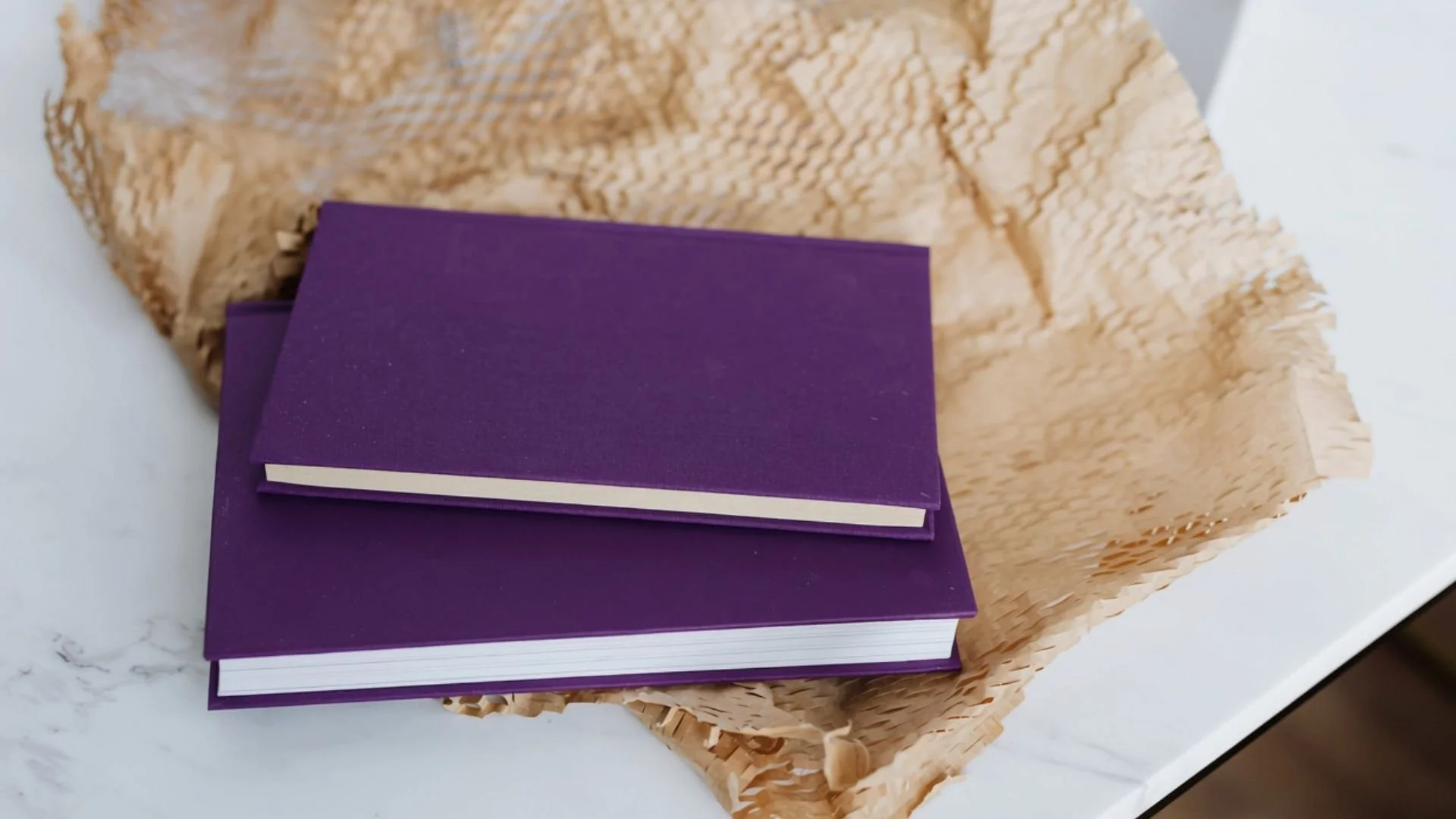 Purple closed notebook placed on a straw-wrapped rectangular box, on a white surface.