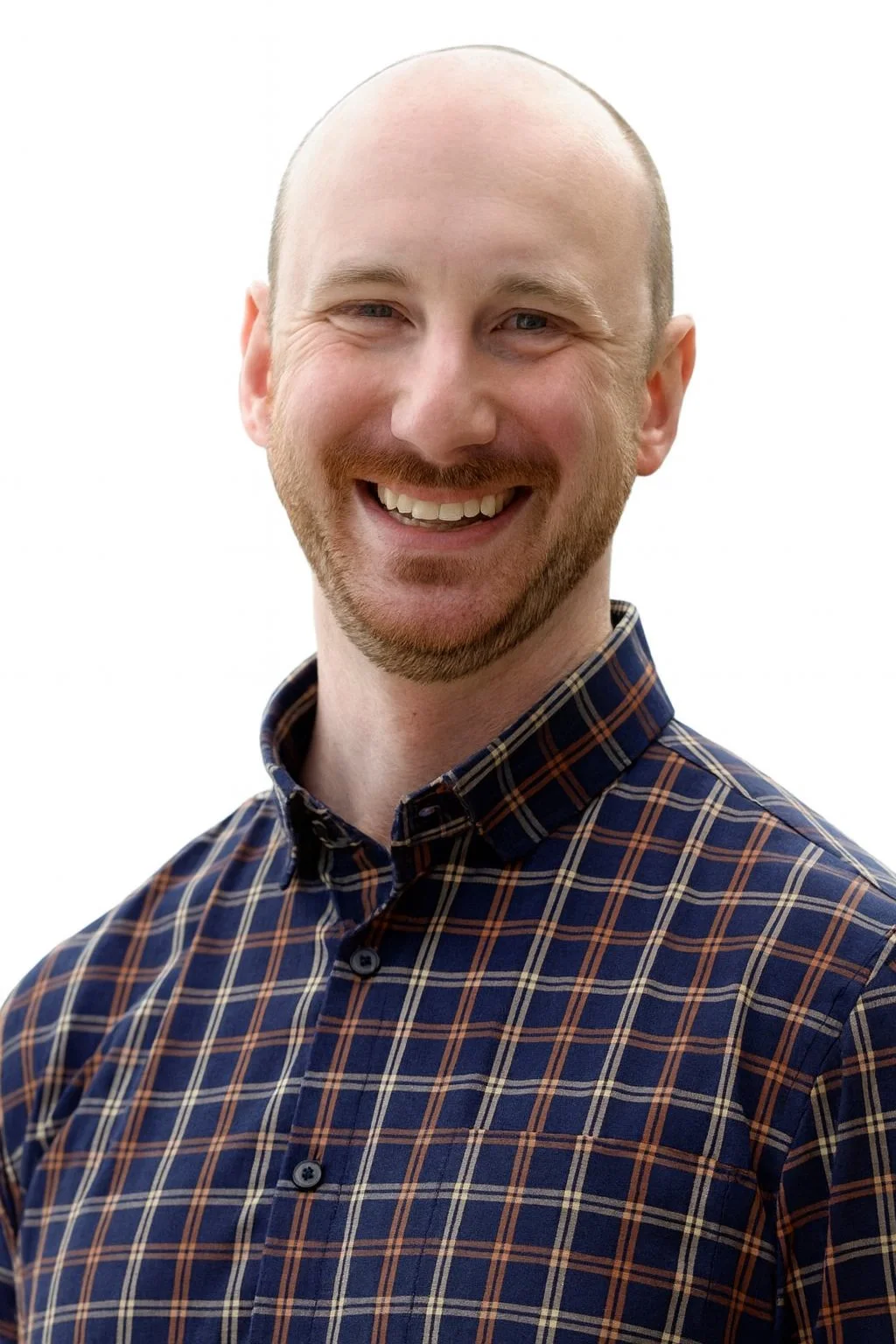 A smiling man with a beard and bald head wearing a plaid shirt. The background is plain white.