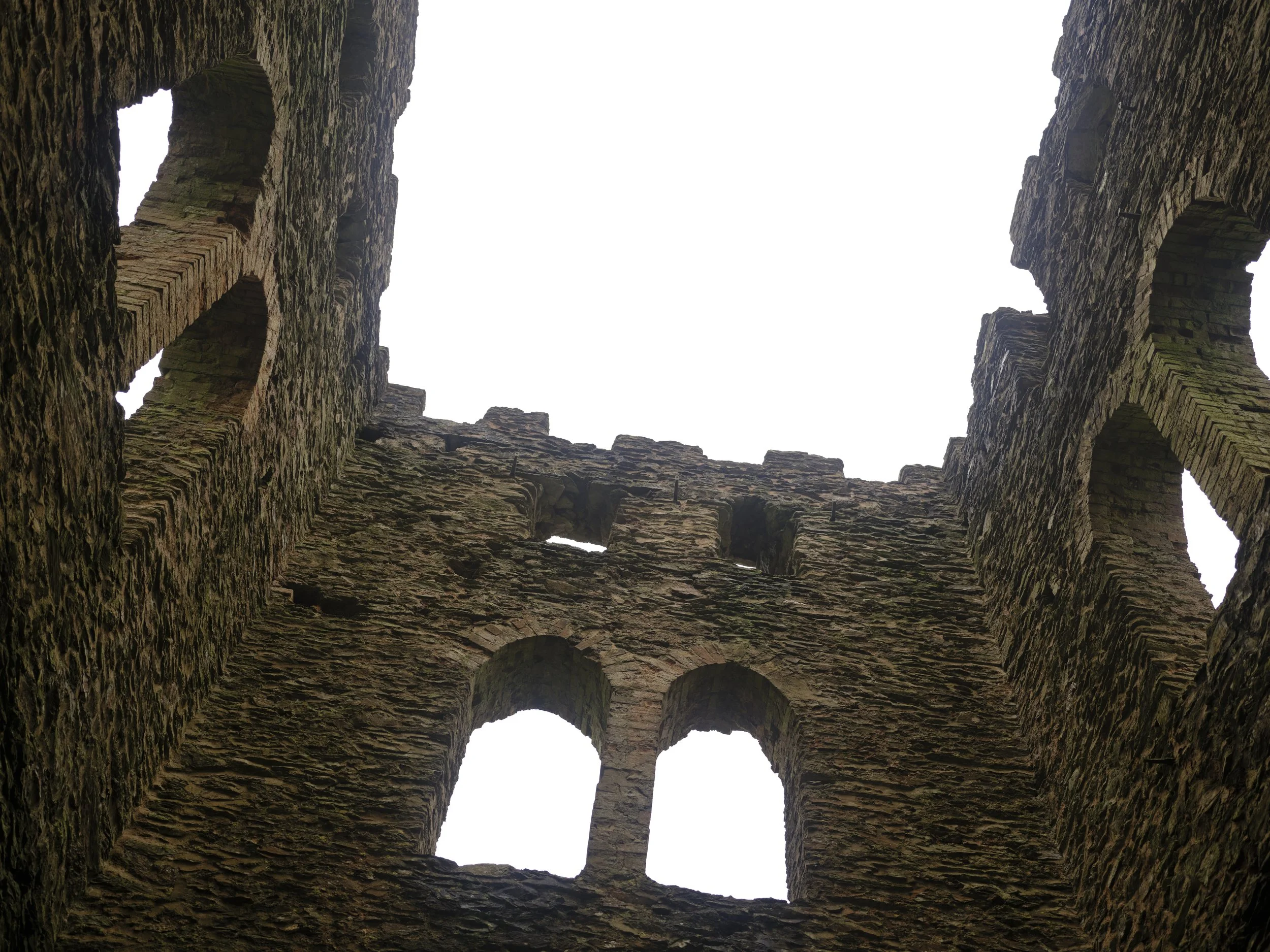 View from inside of an ancient brick castle looking up through the open roof to a cloudy sky.