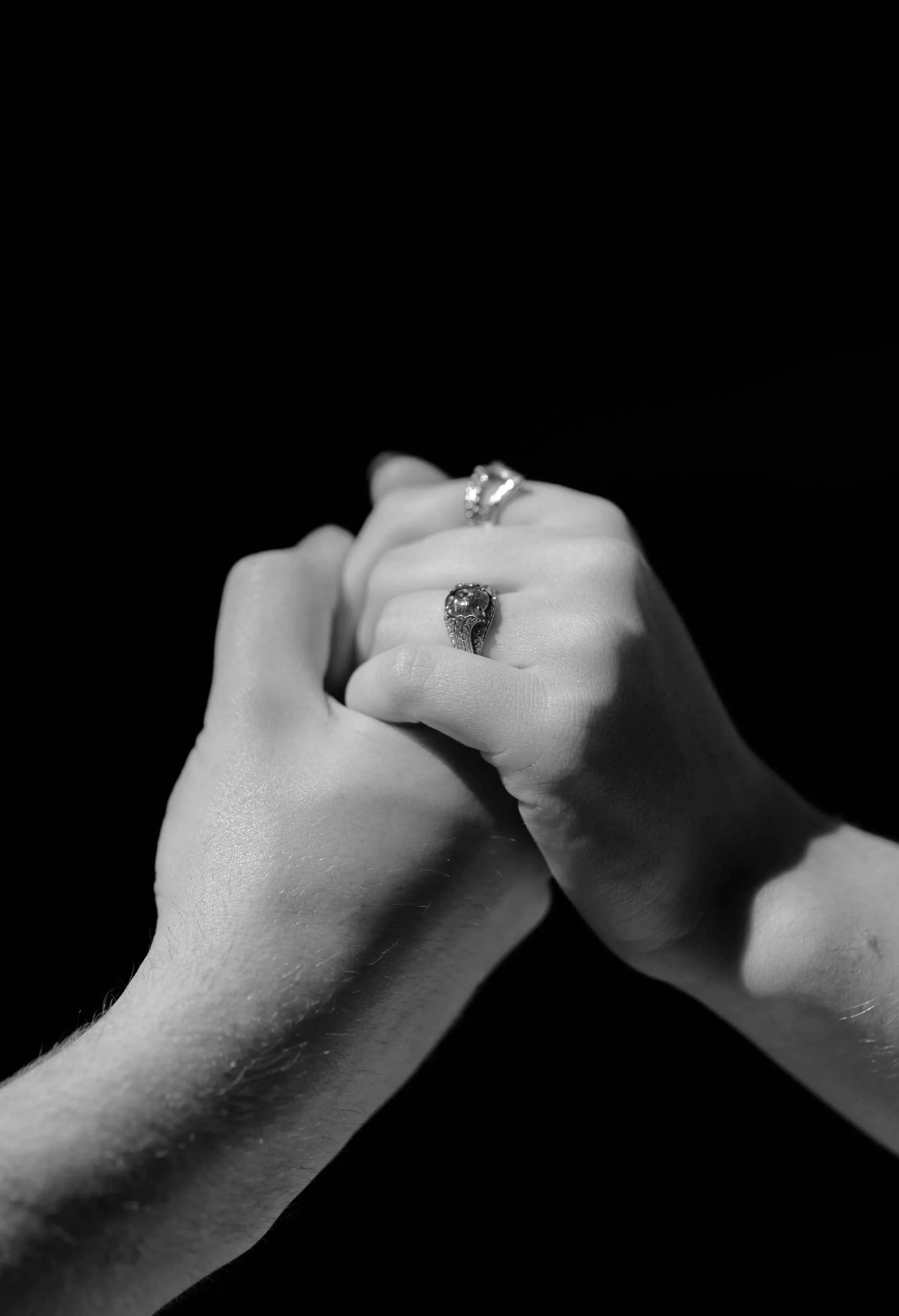 Close-up of two hands with rings against a black background.