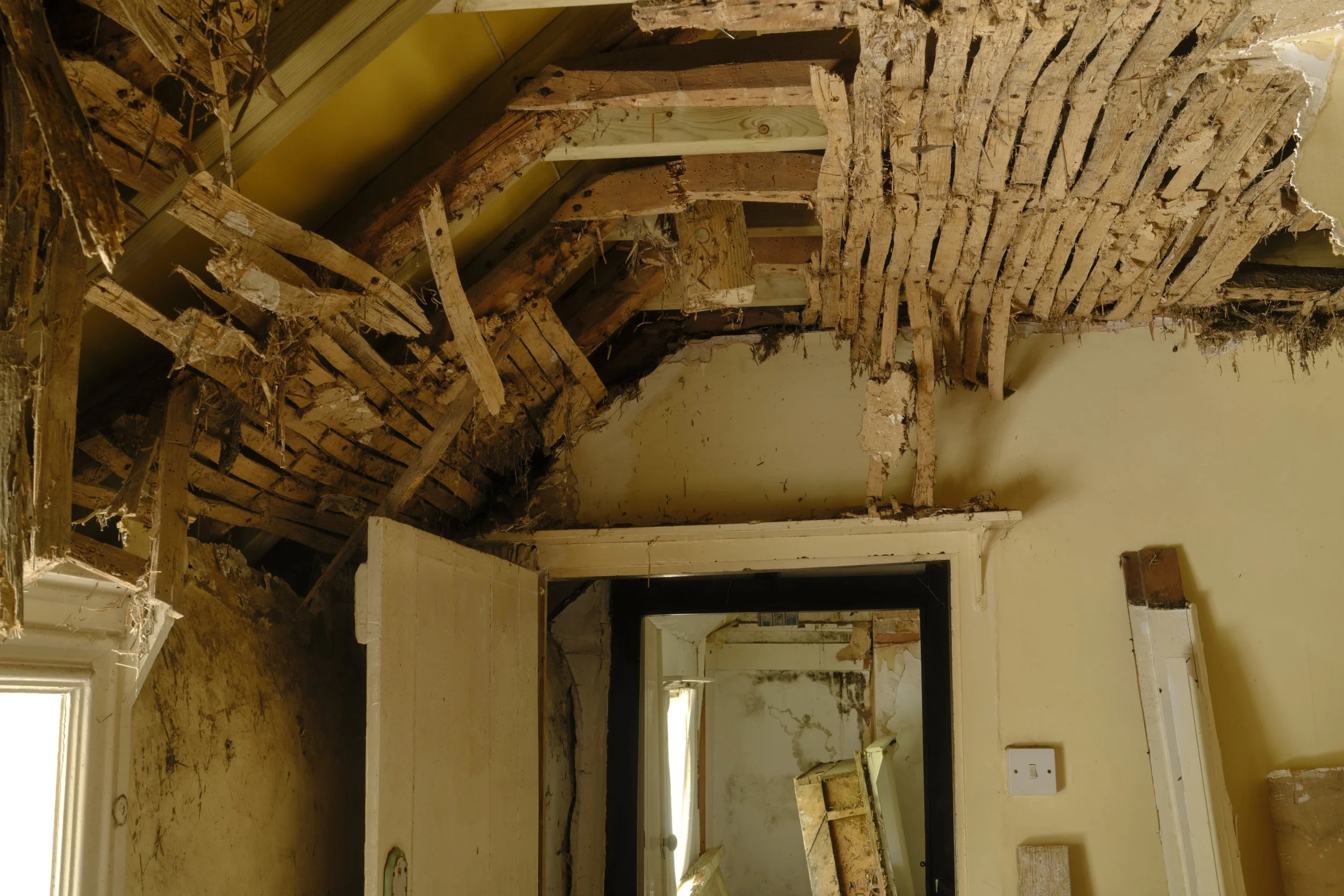 A room undergoing renovation with exposed wooden wall studs, debris, and construction materials.