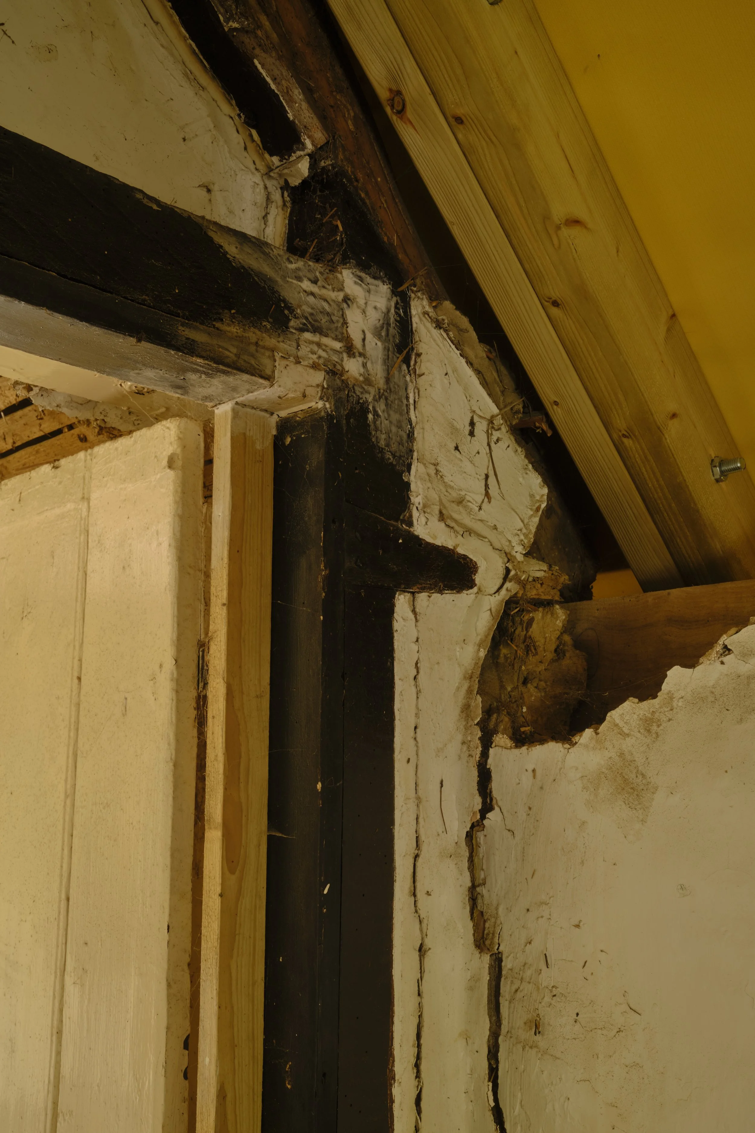 Close-up of a construction area with a wooden plank above a section of black waterproofing membrane, showing exposed wall and foundation with signs of damage and cracks.