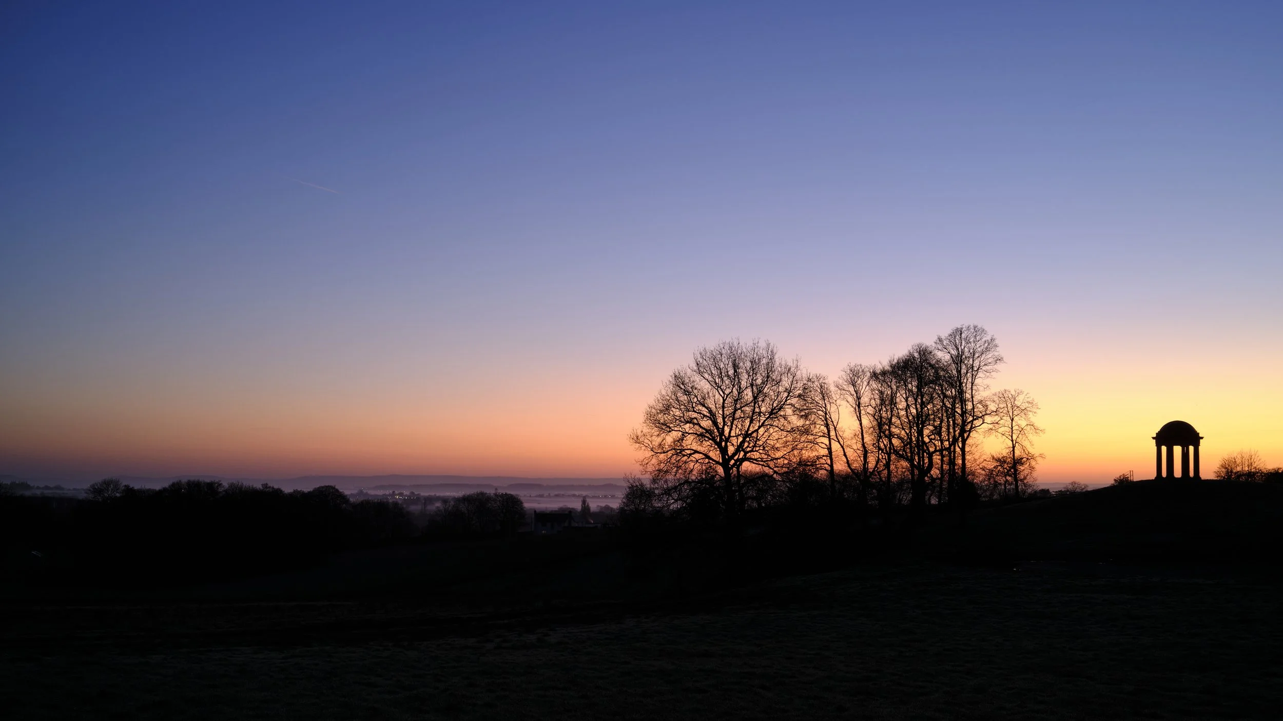Copyright Laurence Cummins Photography/Halswell Park - Silhouette of trees and a small pavilion against a colorful sunrise or sunset sky with gradient hues of blue, pink, orange, and purple.