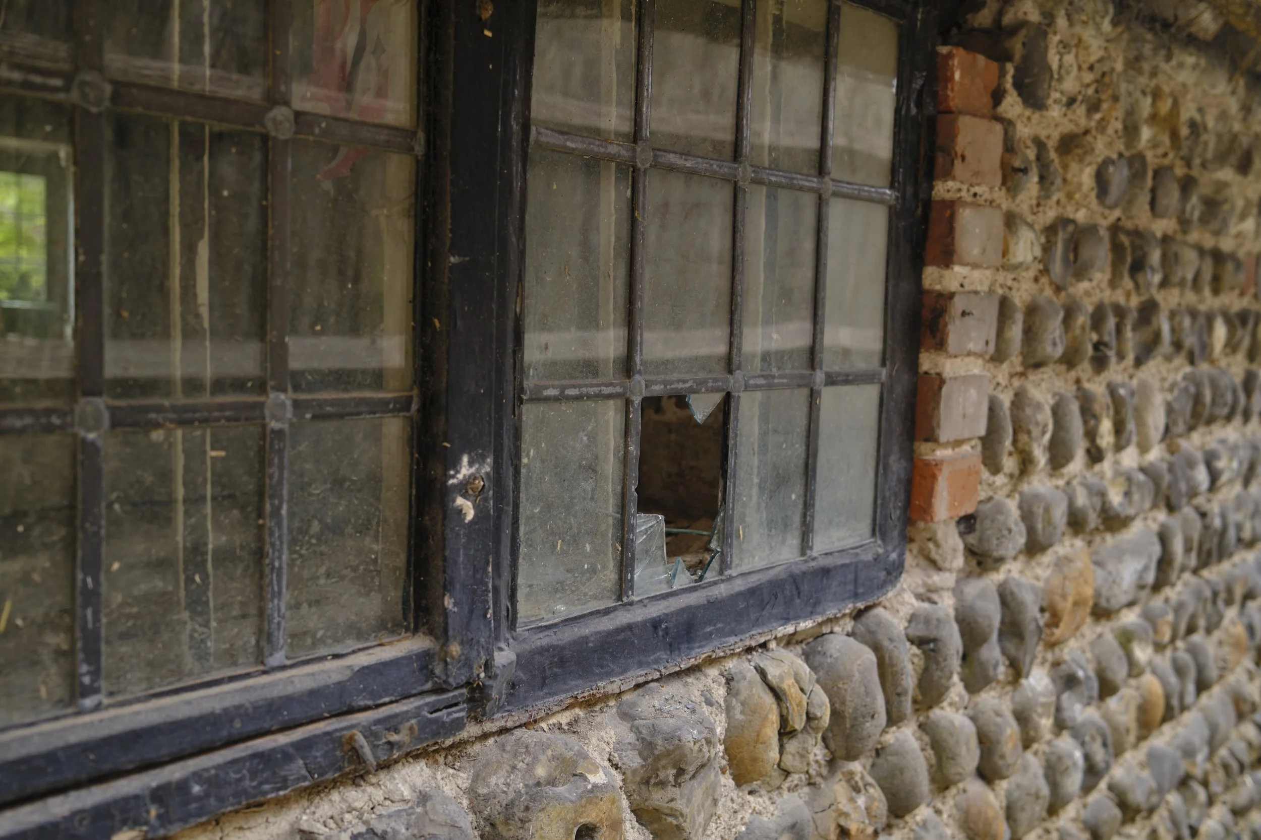 Broken window with metal bars in front of a stone and brick wall.