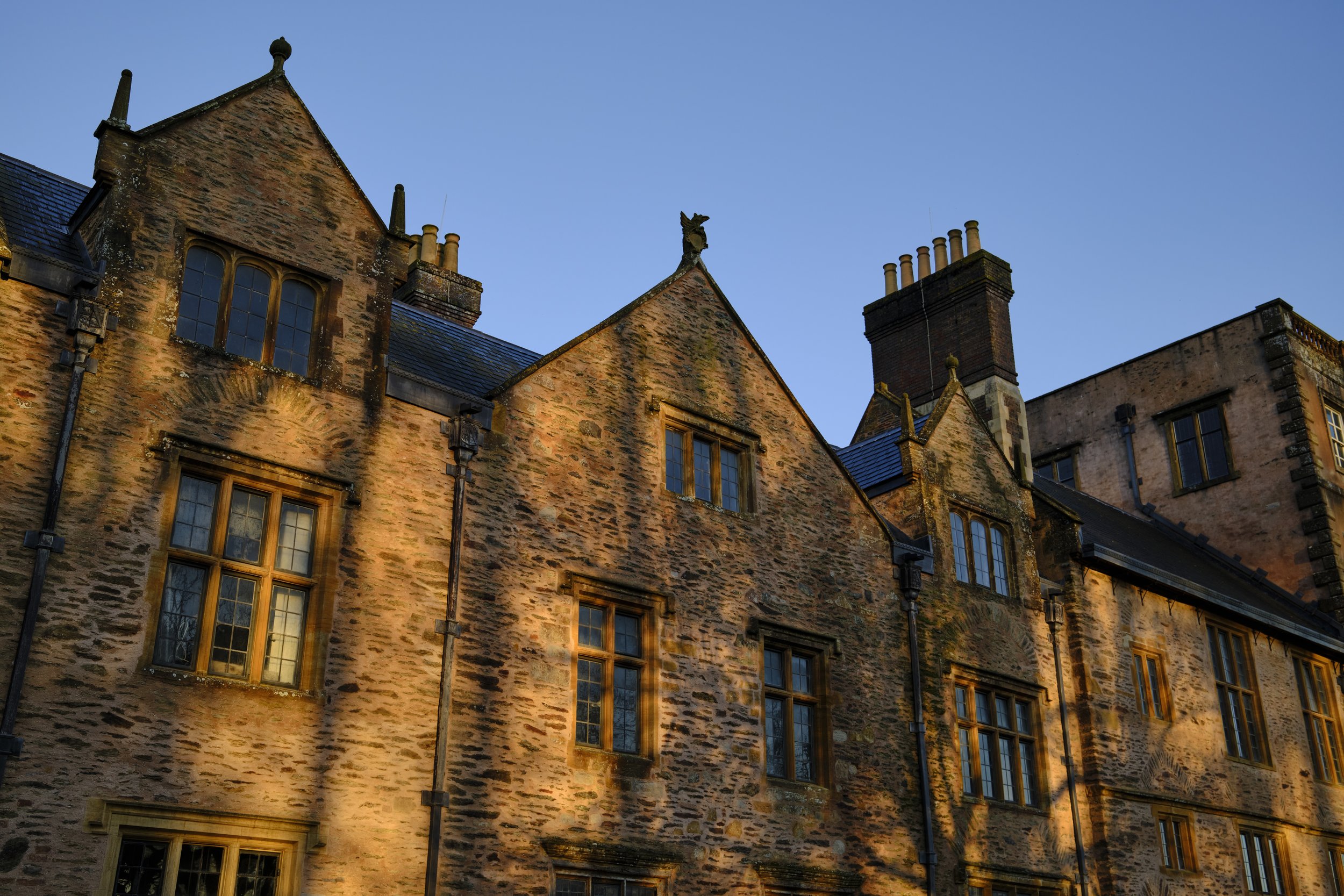 Copyright Laurence Cummins Photography / Halswell Park - Old stone building with multiple windows and chimneys, bathed in warm sunlight, under a clear blue sky.