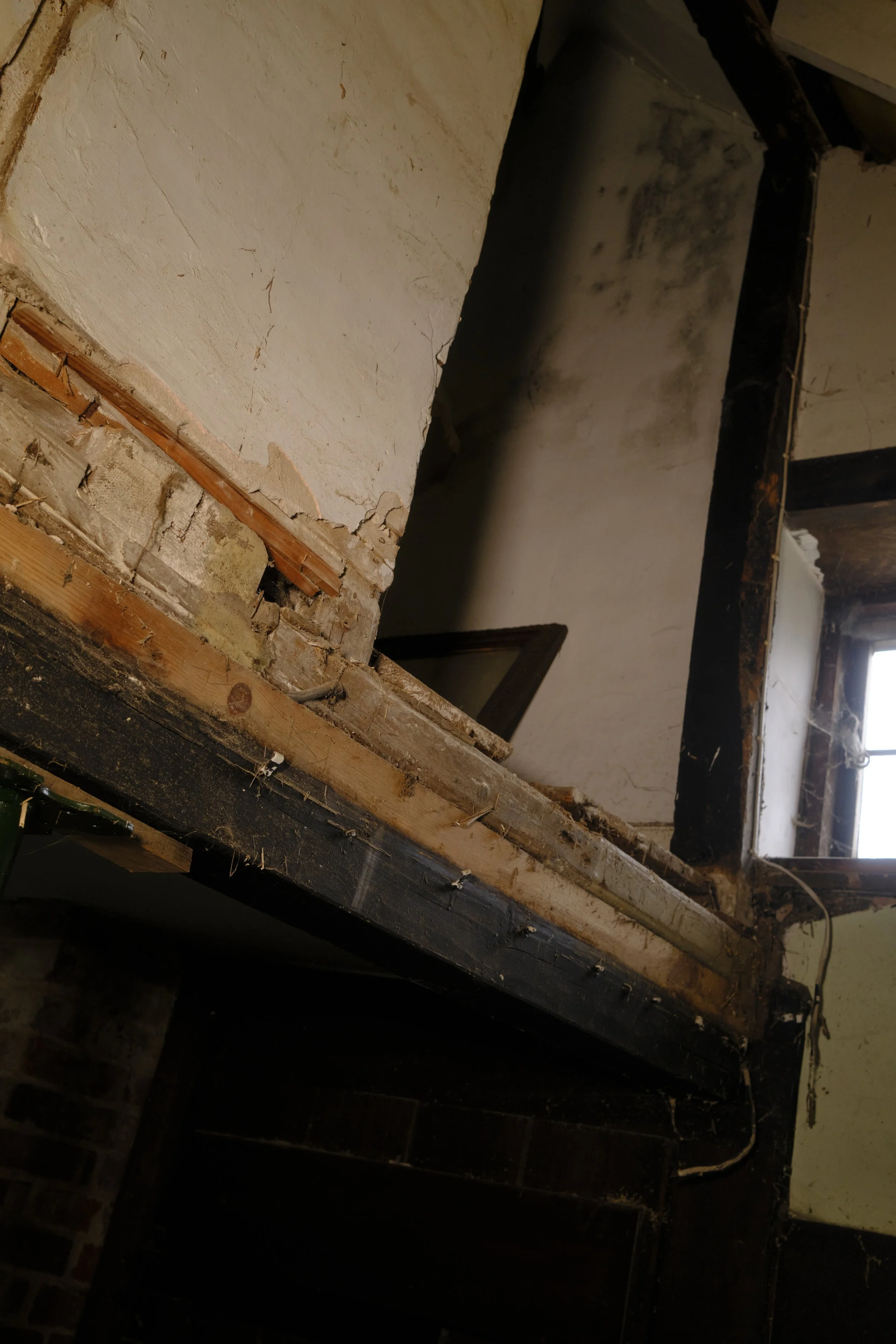 A partially demolished interior wall with exposed wooden beams, bricks, and damaged drywall, indicating renovation or construction work.