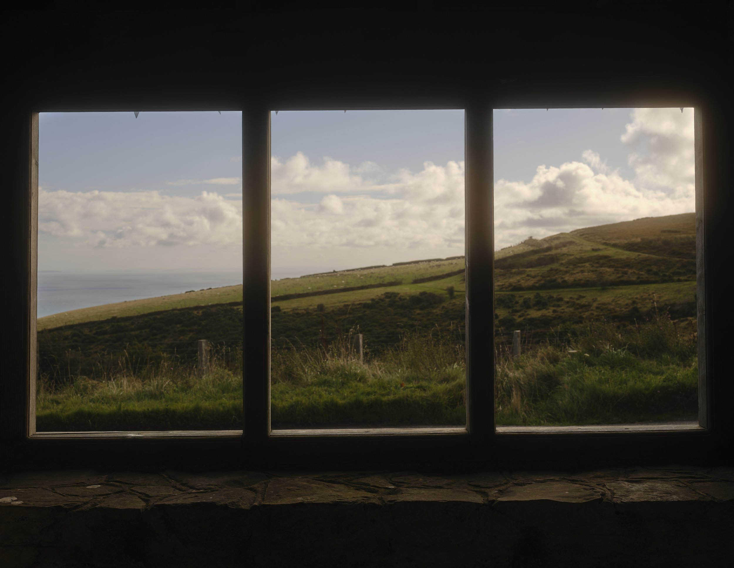 Scenic view of green hills, cloudy sky, and a body of water seen through a window with four vertical bars.