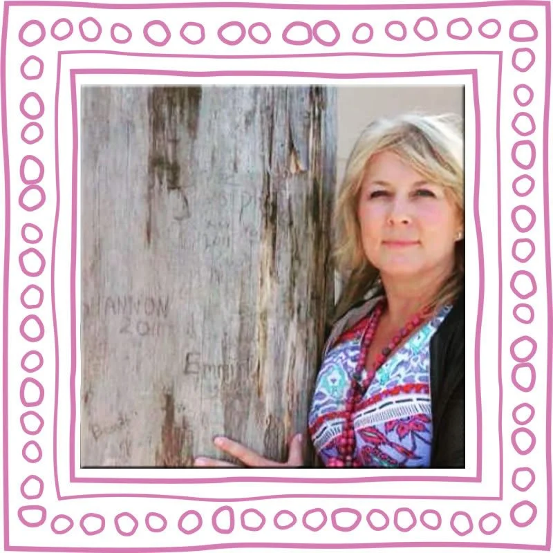 Woman with blonde hair standing beside a weathered wooden post with carved names and dates