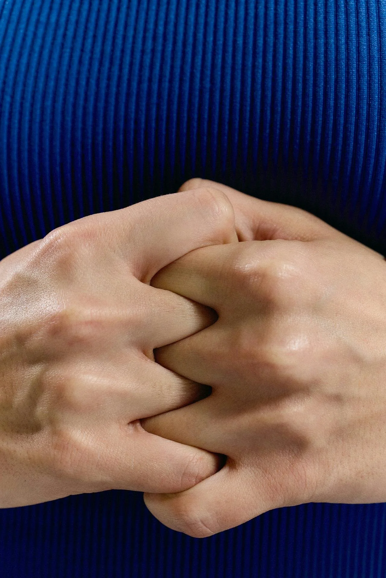 Close-up photo of two people holding hands with interlocked fingers against a blue ribbed fabric background.