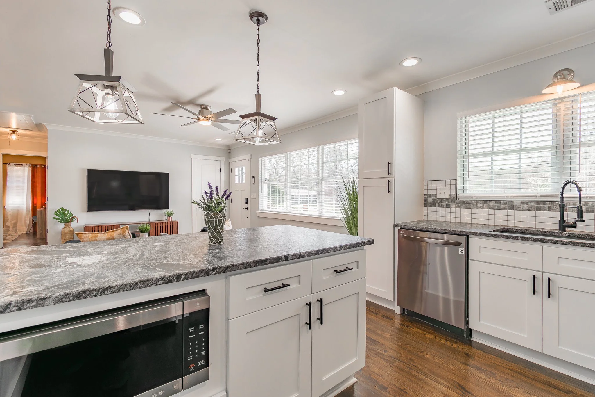 Modern kitchen with white cabinets, granite countertops, stainless steel appliances, and large windows letting in natural light.
