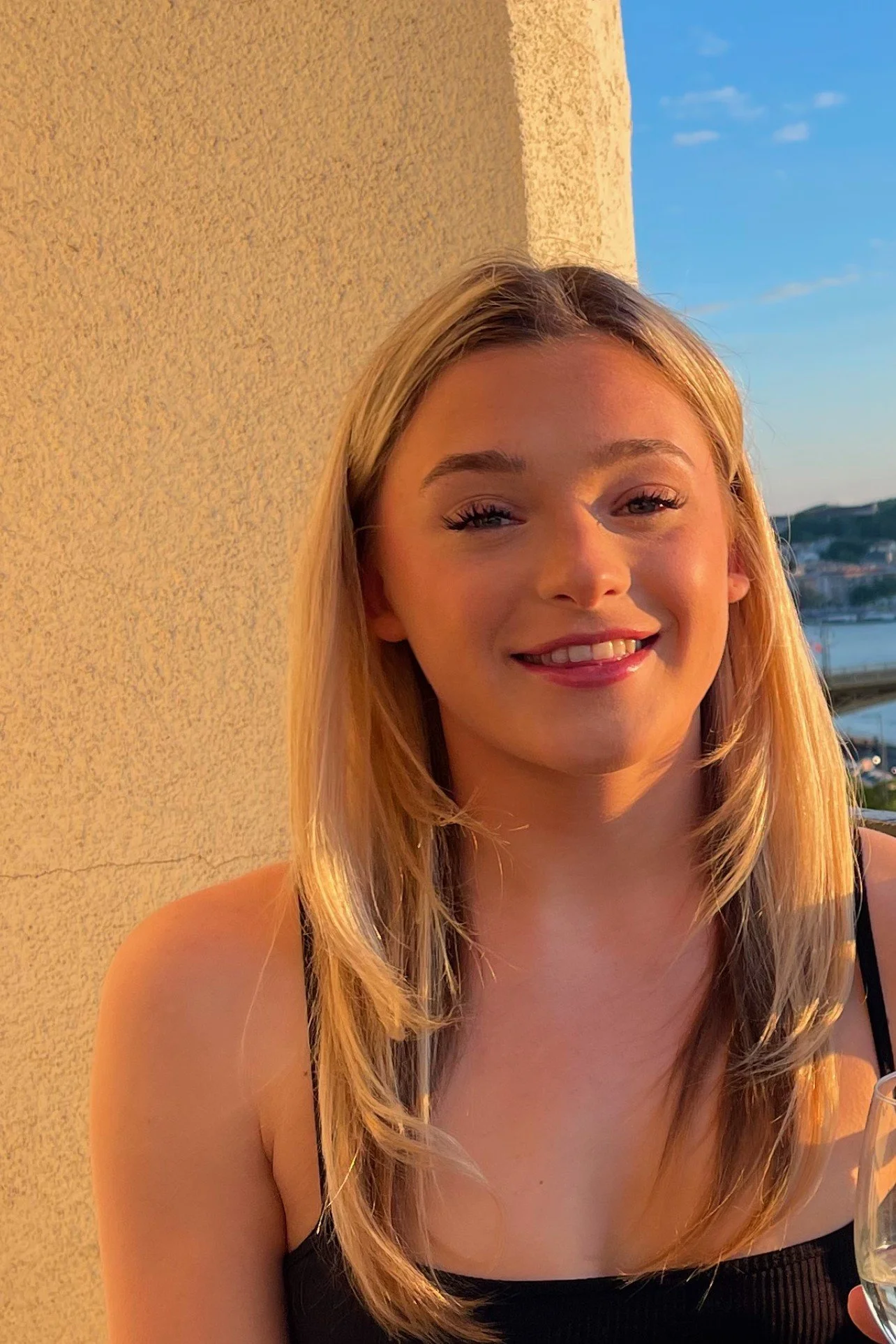 Young woman with blonde hair smiling outdoors during sunset.