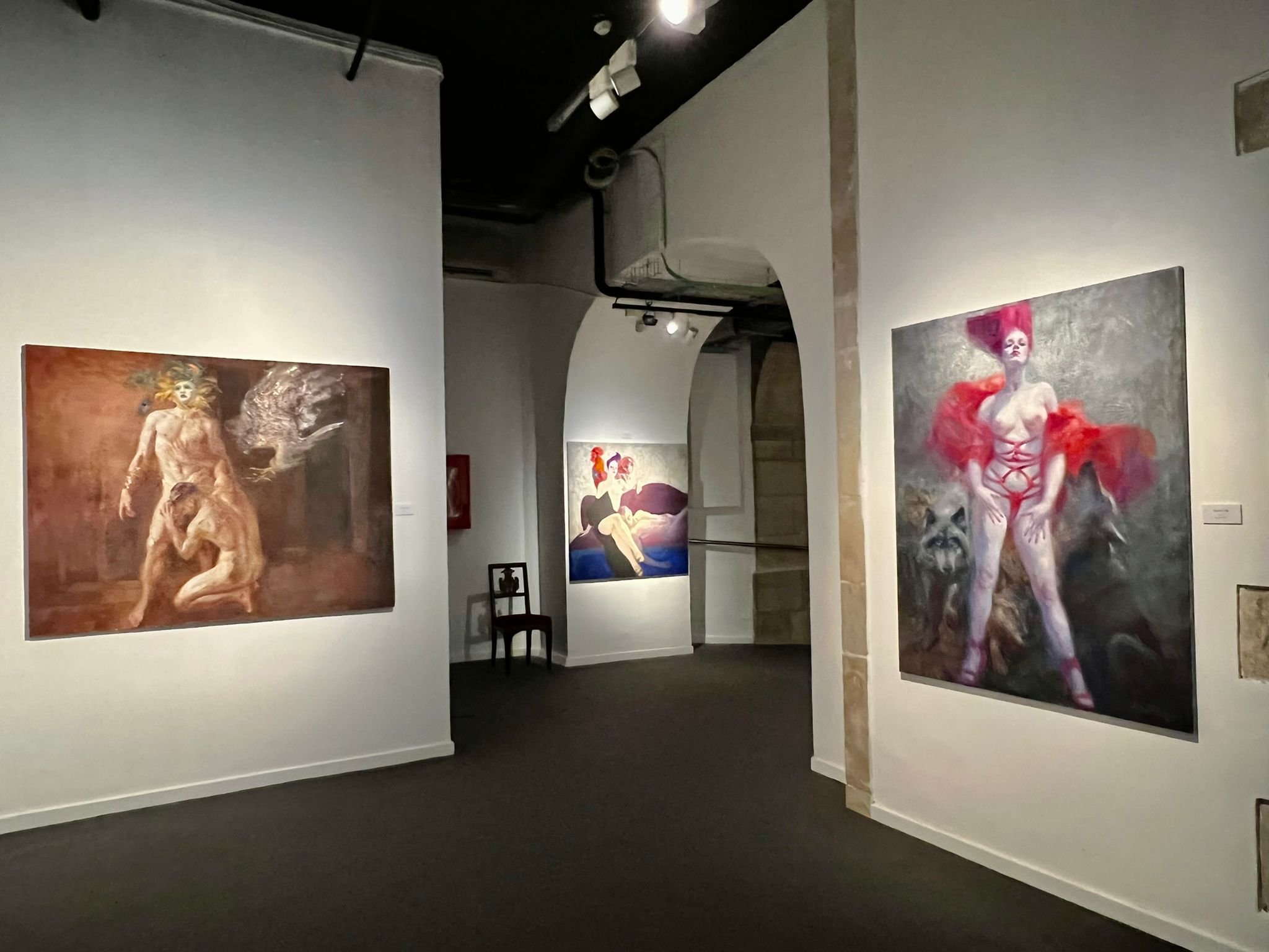 An art gallery with paintings on the walls, featuring fantasy and surreal themes, including a woman with red hair and abstract figures.