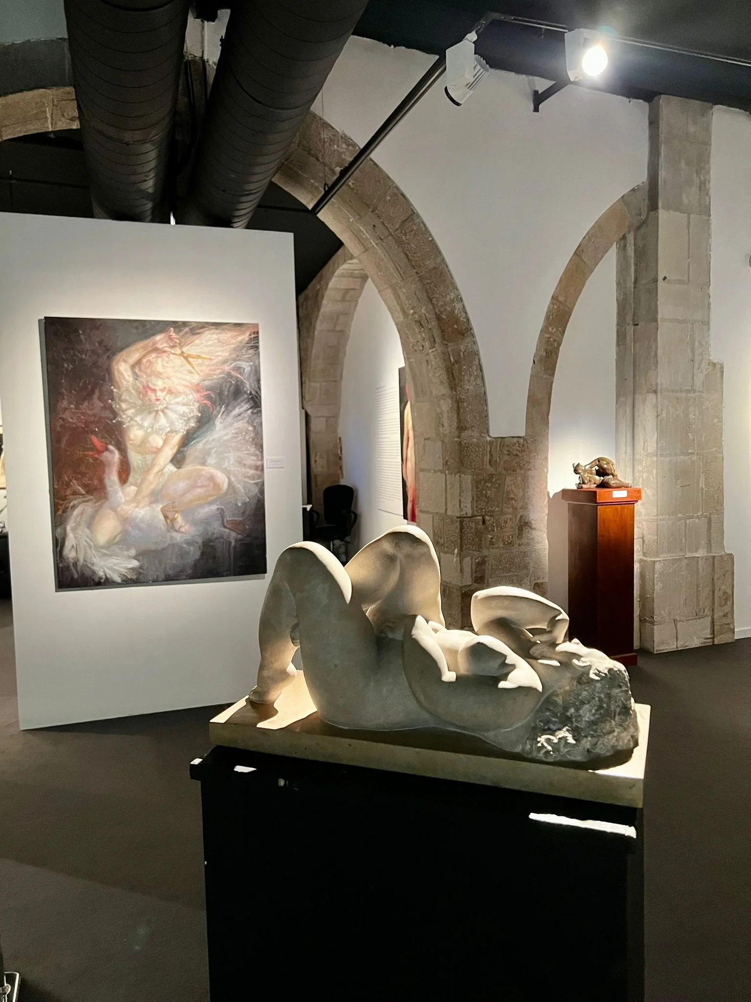 Art gallery displaying sculptures and paintings, with stone arches and dim lighting.