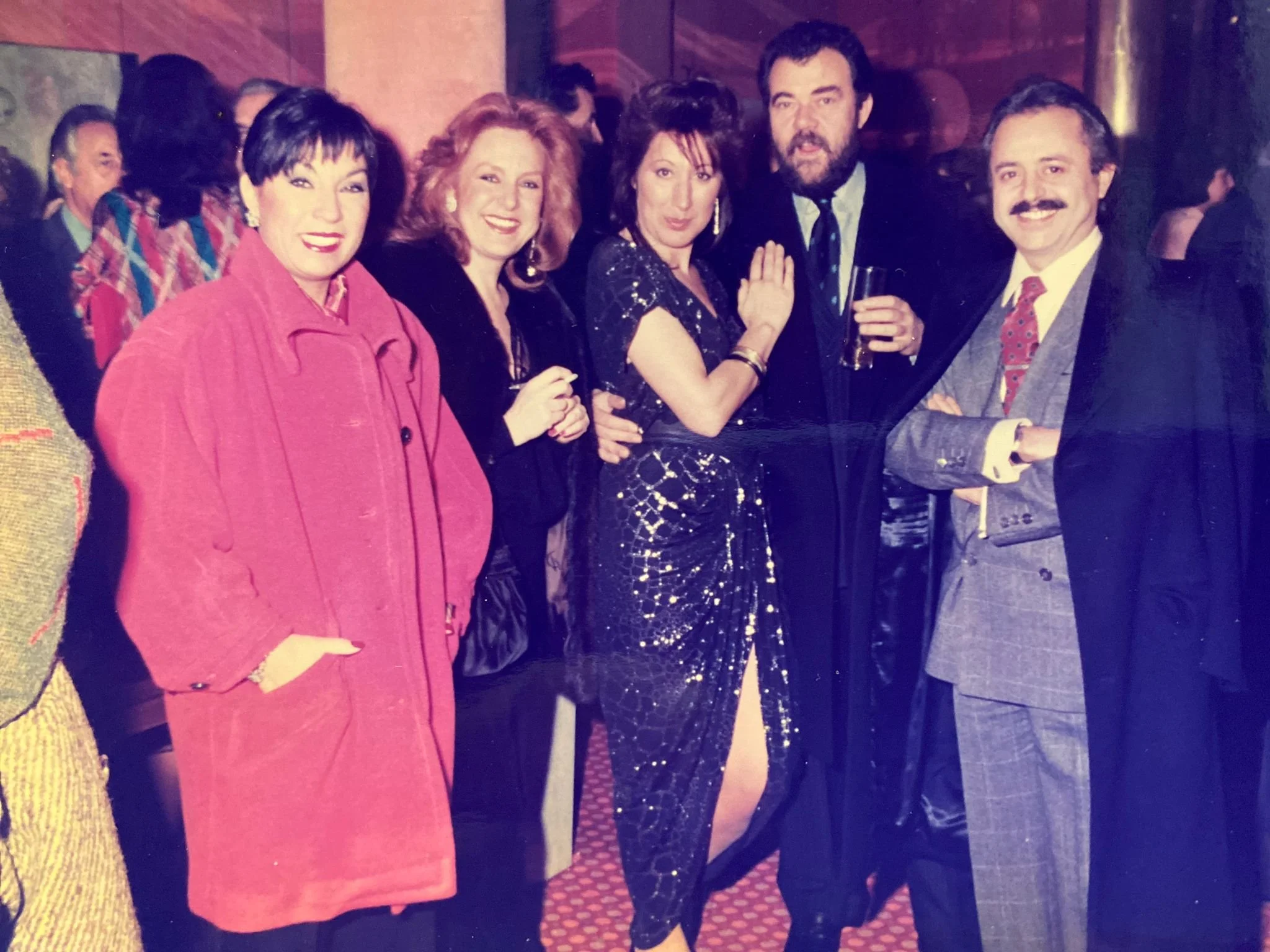 Group of adults dressed in formal and party attire at a social gathering, smiling and posing for the photo.