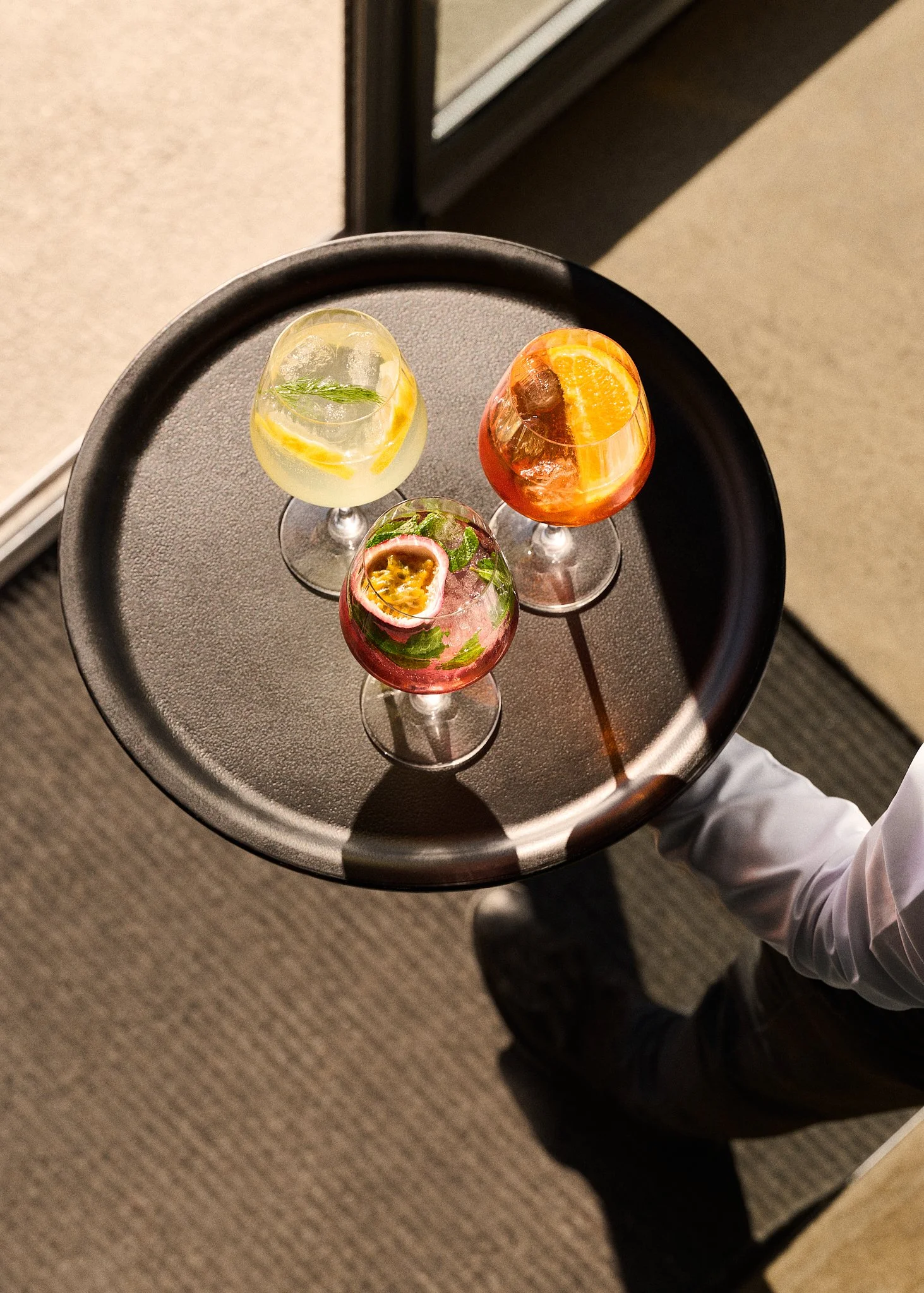 Trois verres de cocktail colorés sur un plateau, tenu par le serveur en chemise blanche.