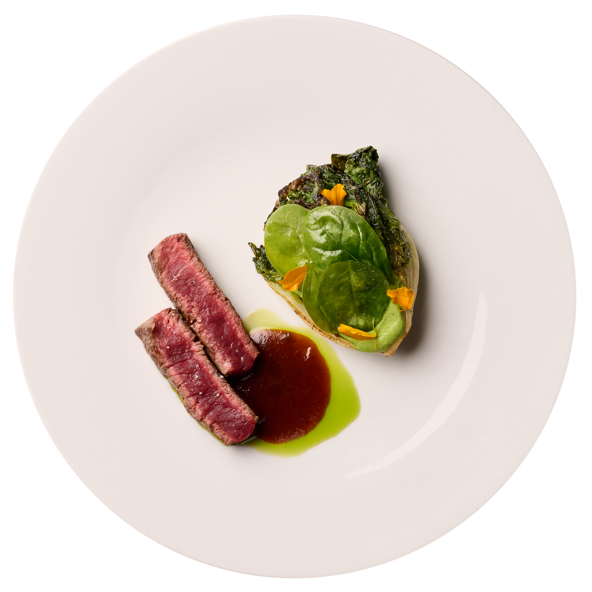 Assiette blanche avec un morceau de viande rouge cuite, une tranche de viande saignante, et une garniture verte avec des fleurs comestibles.