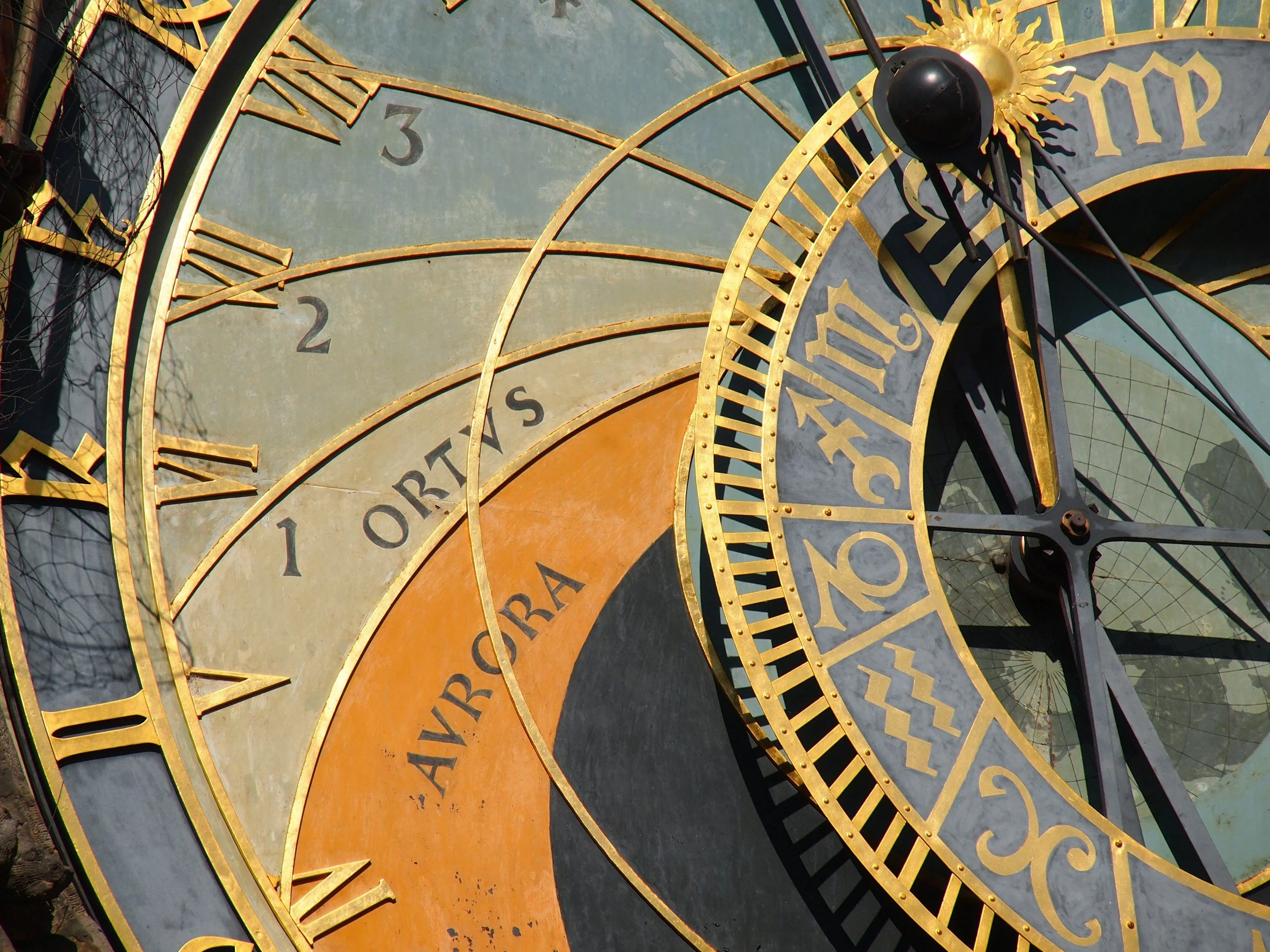 Close-up of an antique clock face showing Roman numerals and intricate gold detailing, with some parts of the clock, like hands and numerals, visible.