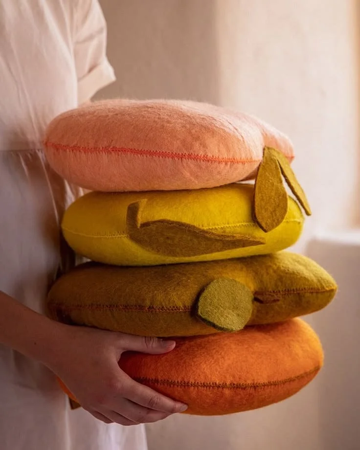 Persona sosteniendo cuatro cojines con forma de pan de queso, con un gato dibujado en los cojines amarillos.