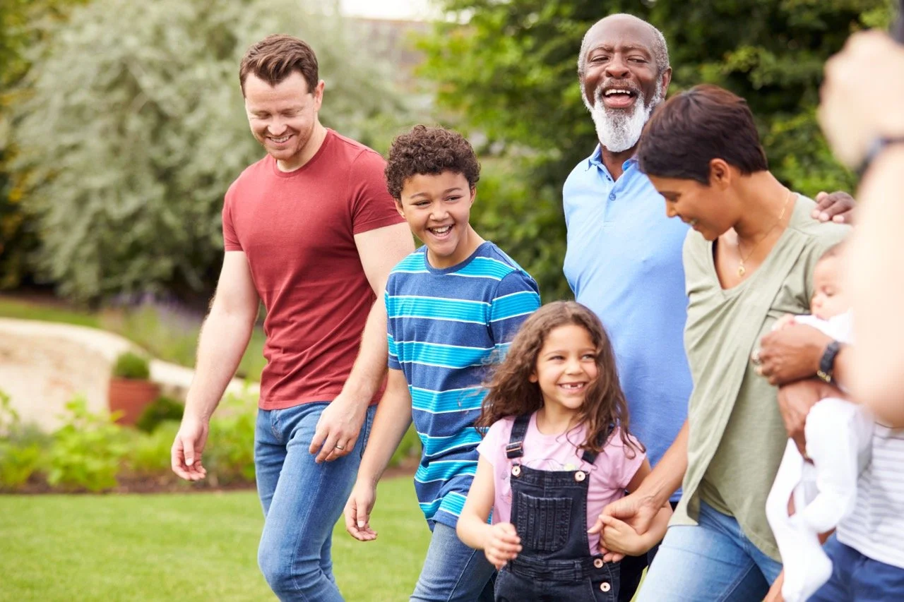 A diverse group of adults and children smiling and playing together outdoors in a park.