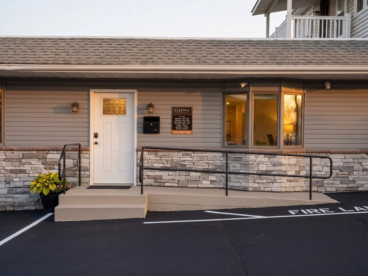 Exterior view of a commercial building with a white door, stone and siding facade, sign for Cleona Chiropractic, and parking spaces labeled 'FIRE LANE'.