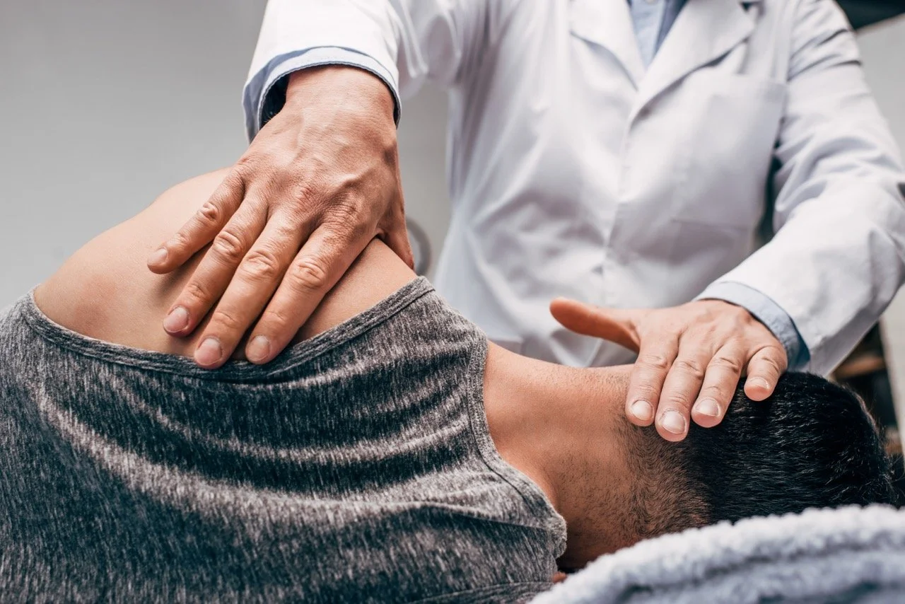 A chiropractor adjusting a patient's neck in a clinic, with the chiropractor wearing a white coat and the patient lying on a treatment table.