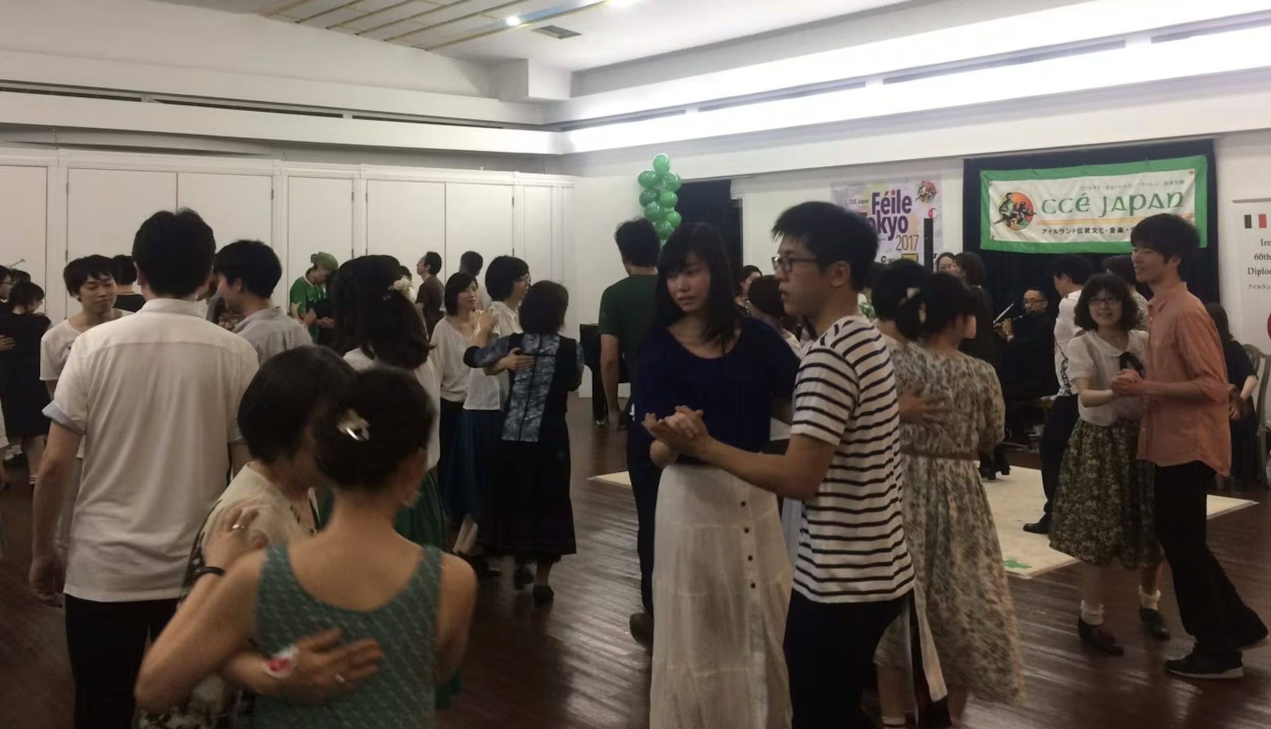 People dancing and socializing at an event with banners and balloons, some in vintage clothing.