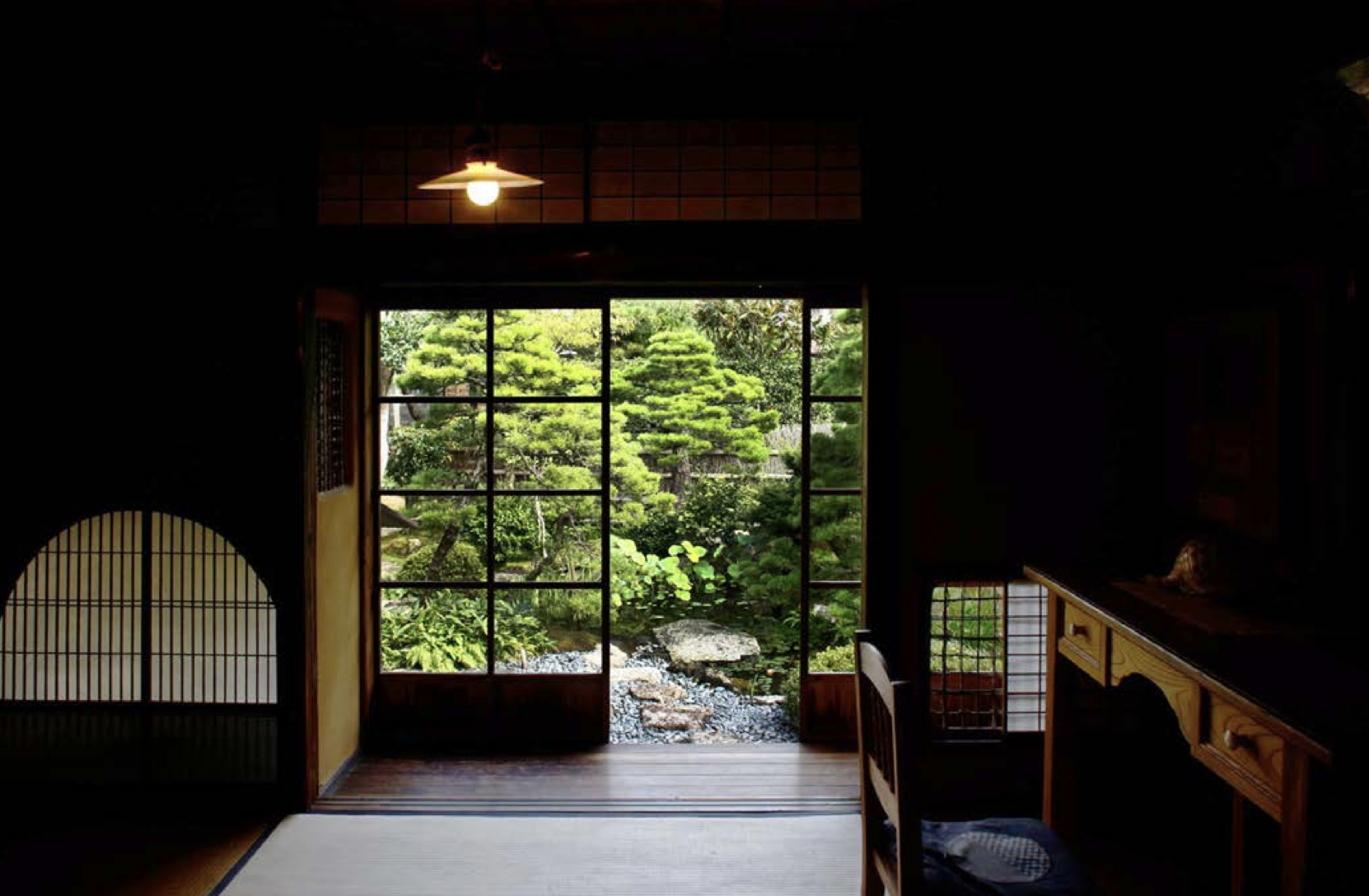 View through sliding glass door of traditional Japanese garden with trimmed trees and rocks.